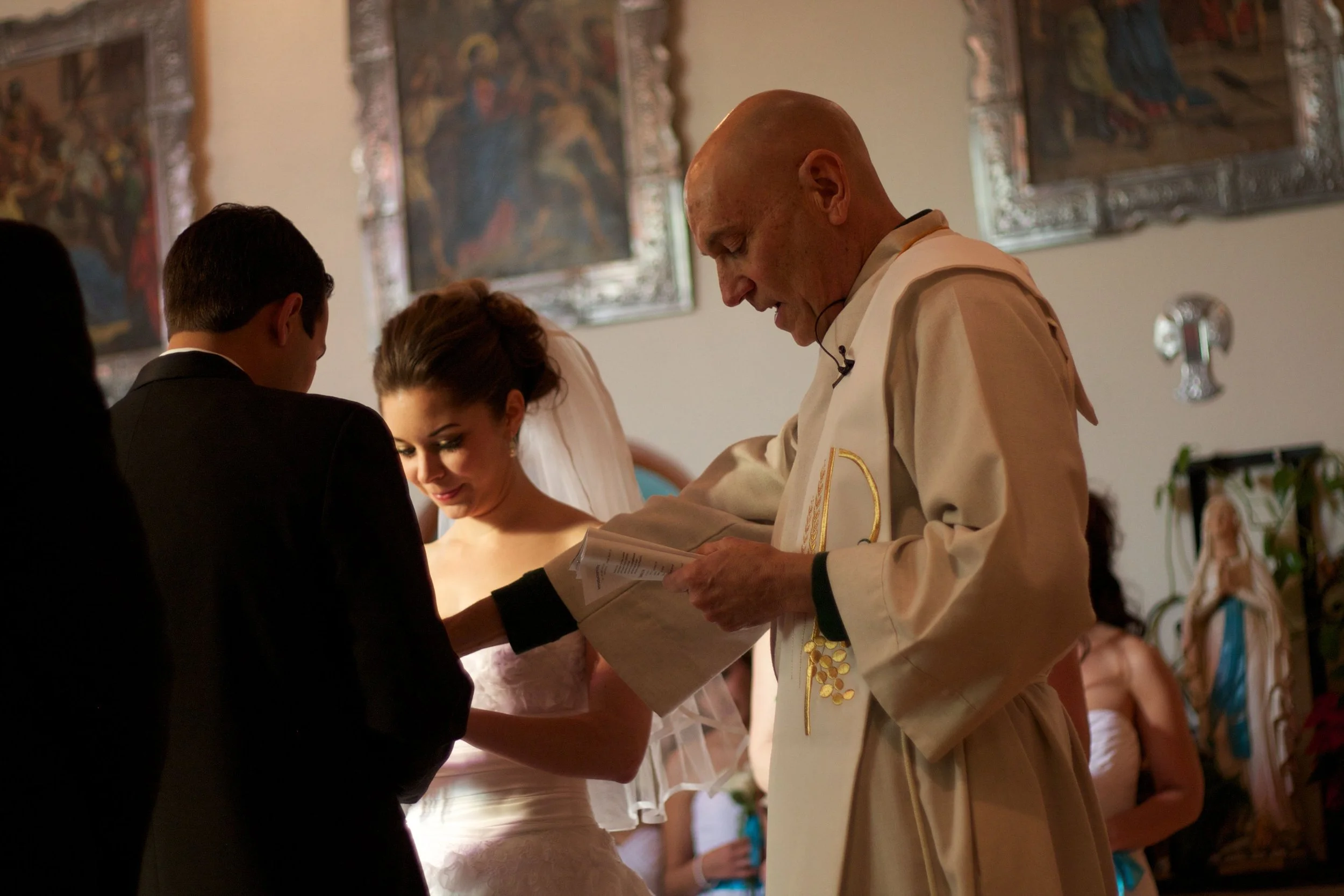A priest officiates a wedding ceremony with a bride and groom, with a priest reading from a book.