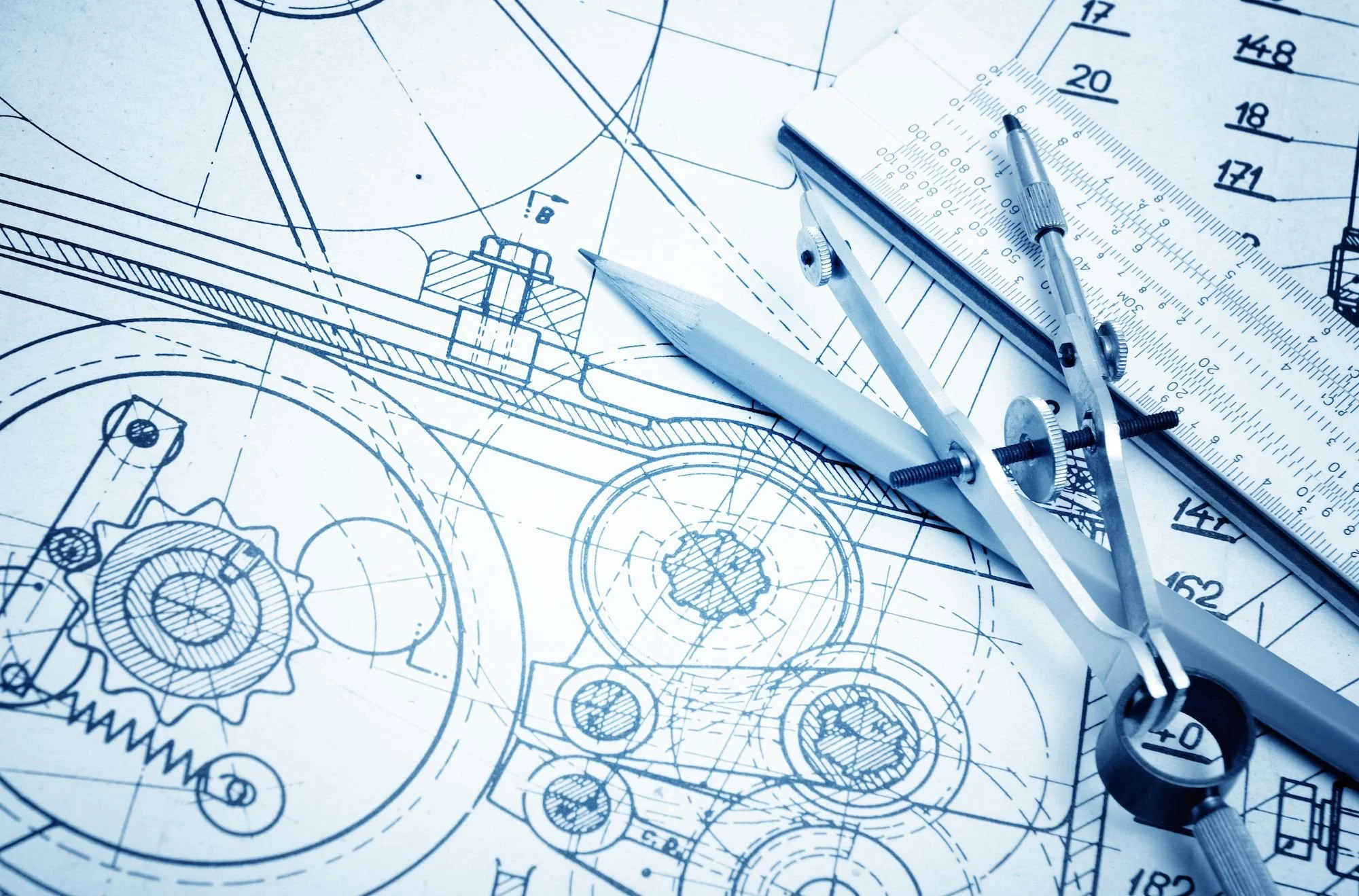 Blueprints of mechanical parts with a compass, ruler, and pencil on top.