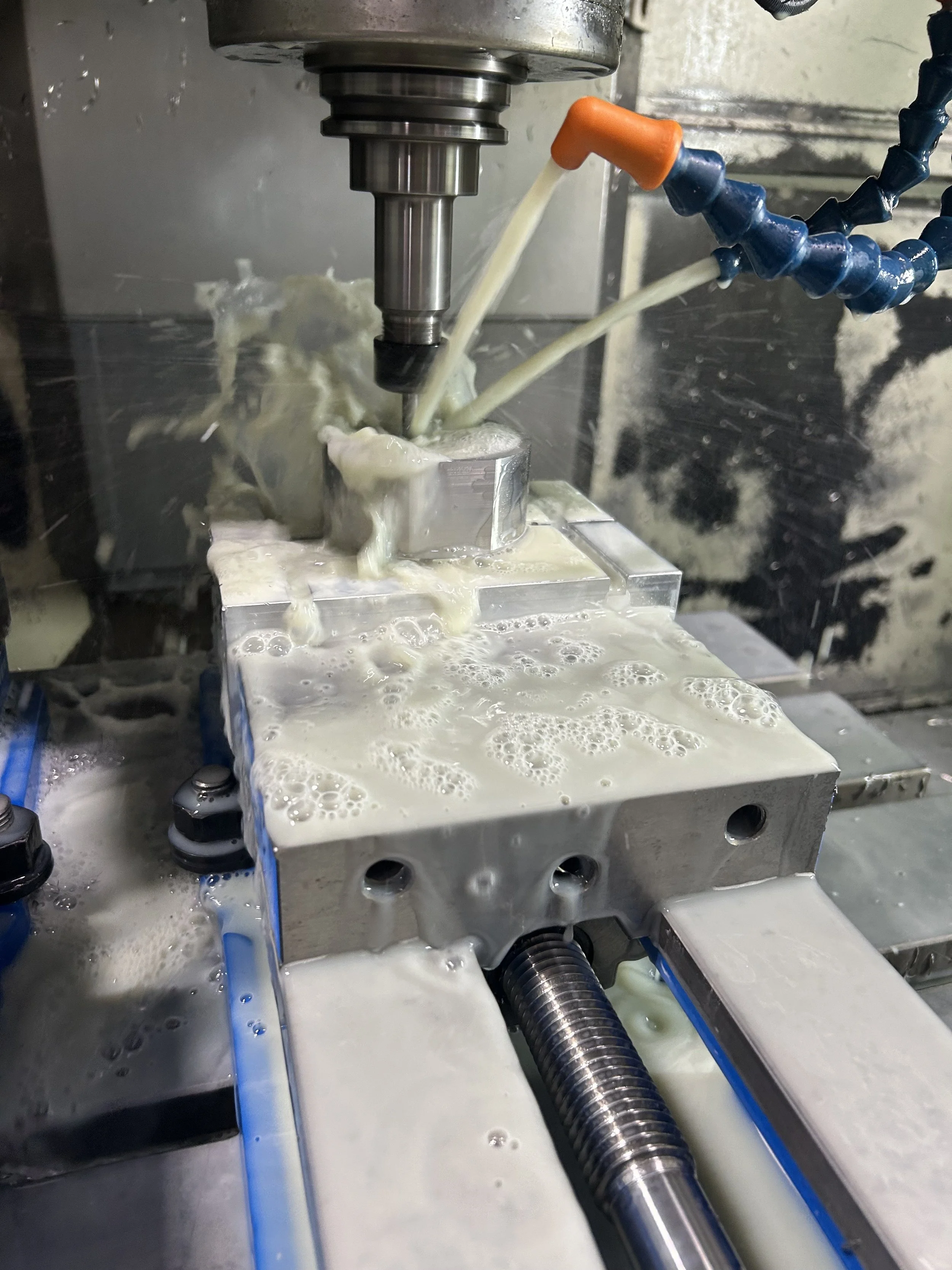 Close-up of a CNC machine milling a metal part with coolant fluid flowing over it.