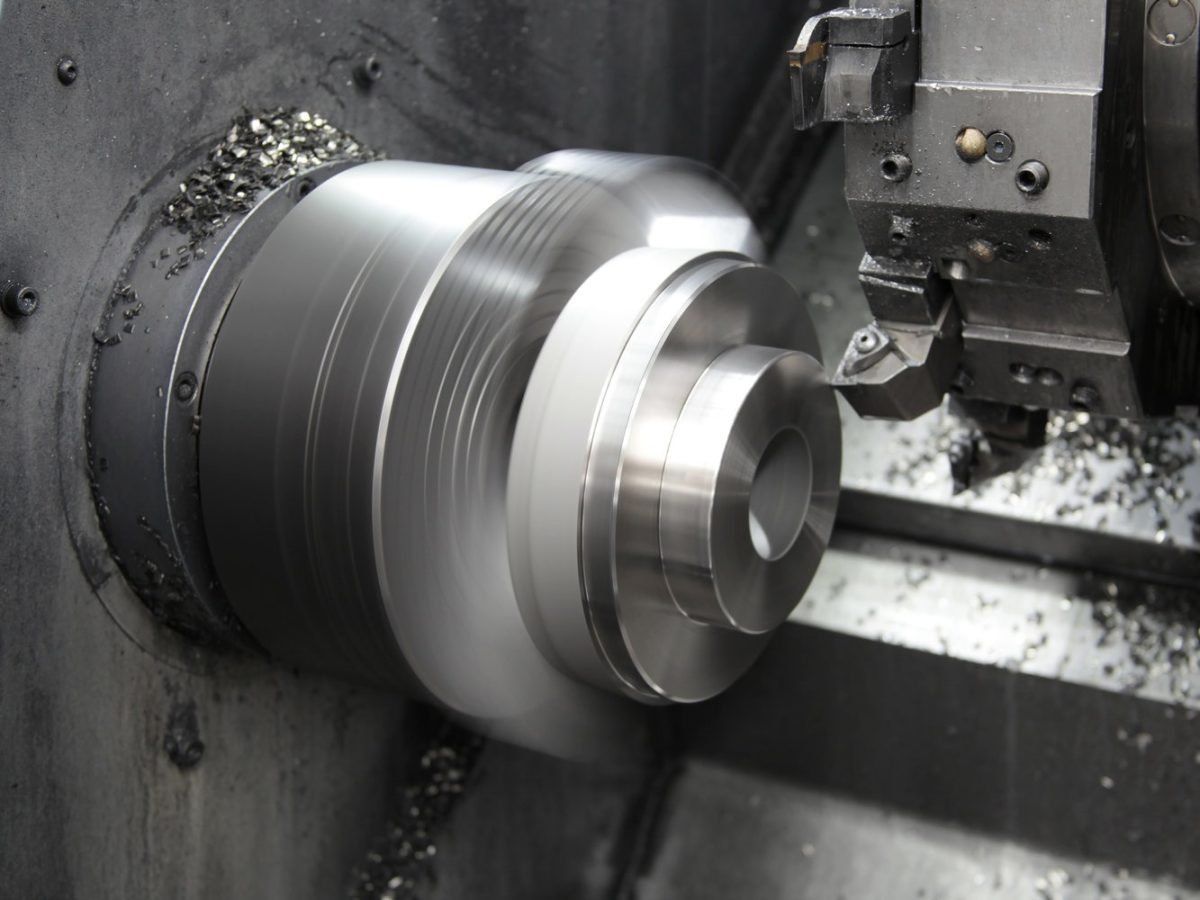 A metal lathe machining a cylindrical metal object, producing metal shavings.