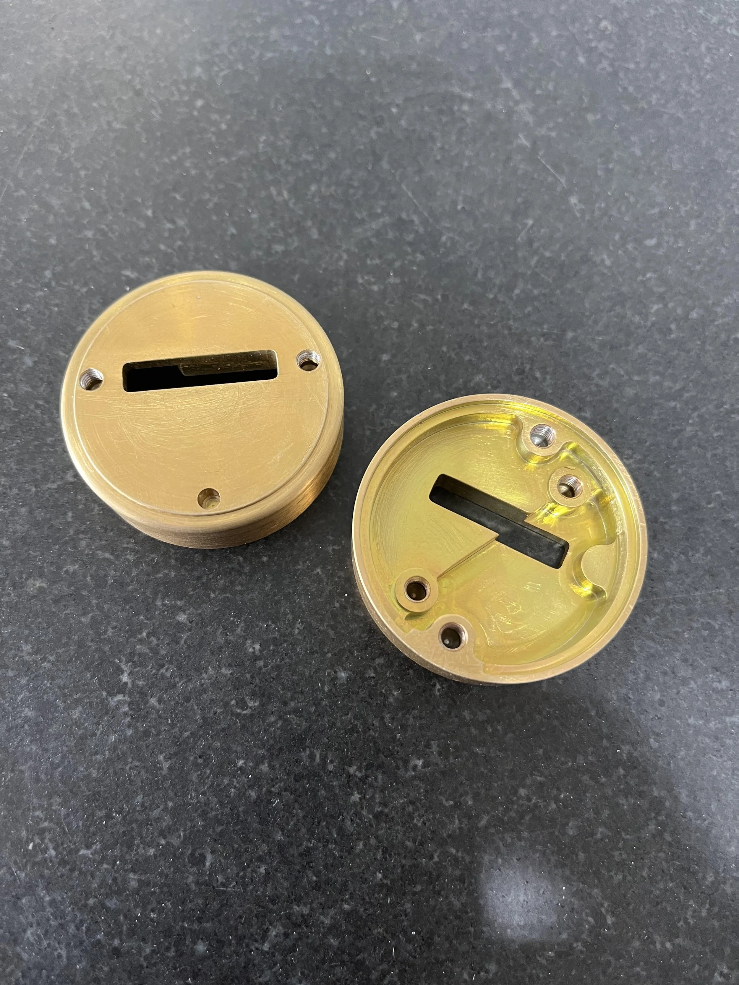 Two gold-colored cylindrical electronic components with black rectangular slots and small screw holes on a dark surface.