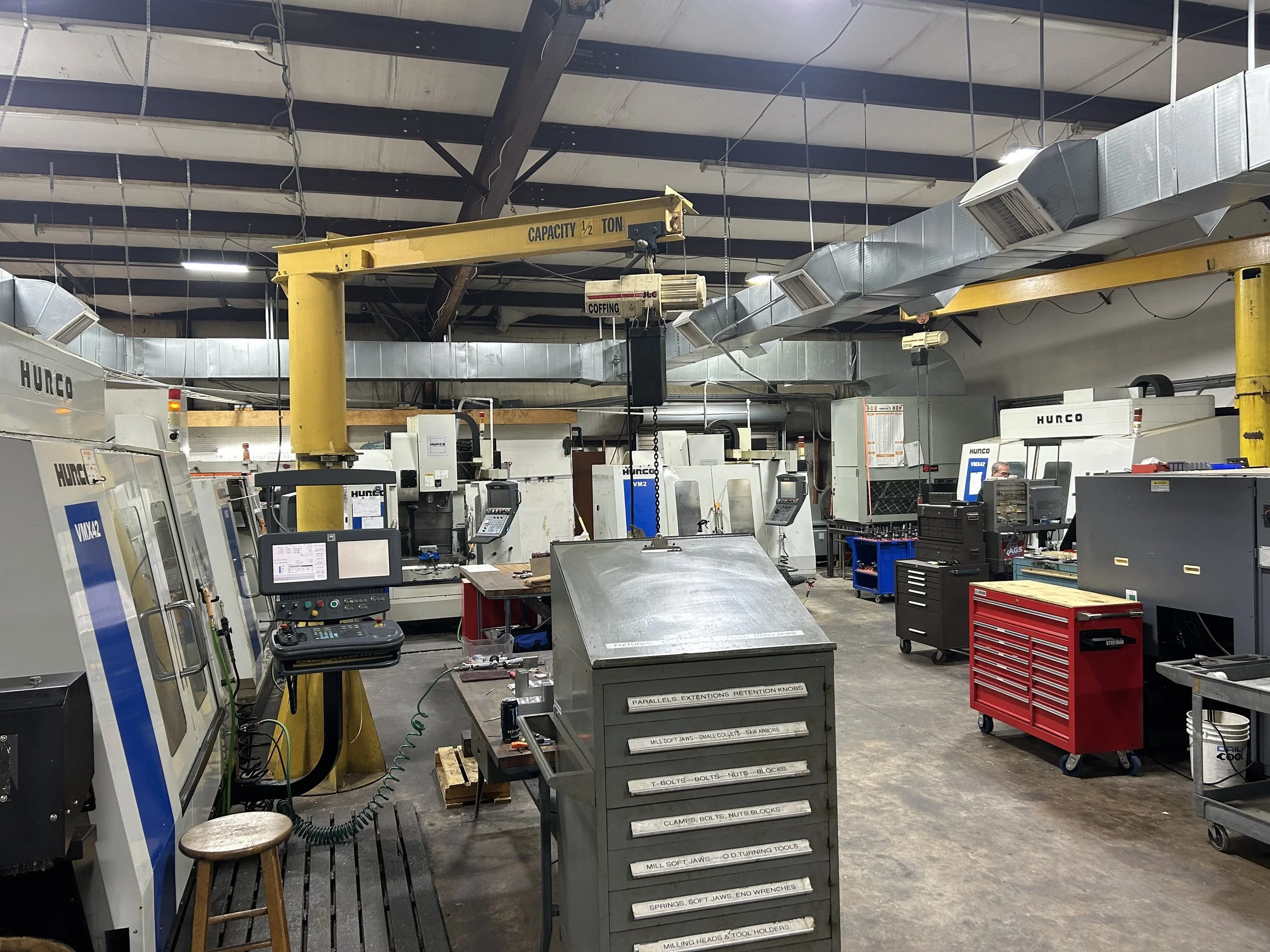 Industrial workshop with multiple CNC machines, tool chests, and a hoist system.