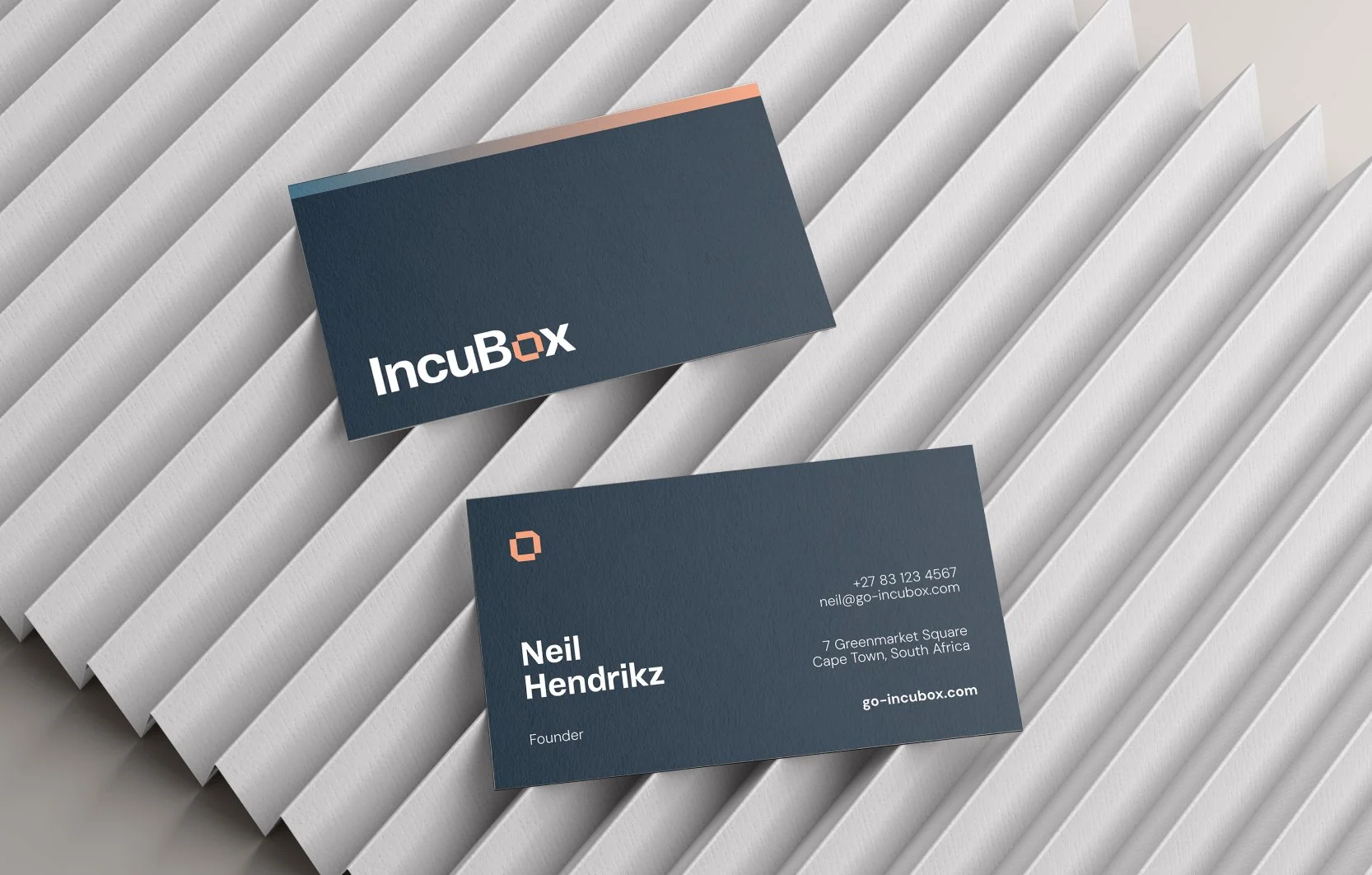 Business cards with a dark navy background, featuring the Incubox logo on one side and contact information for Neil Hendrikz on the other side, placed diagonally on a textured white surface.