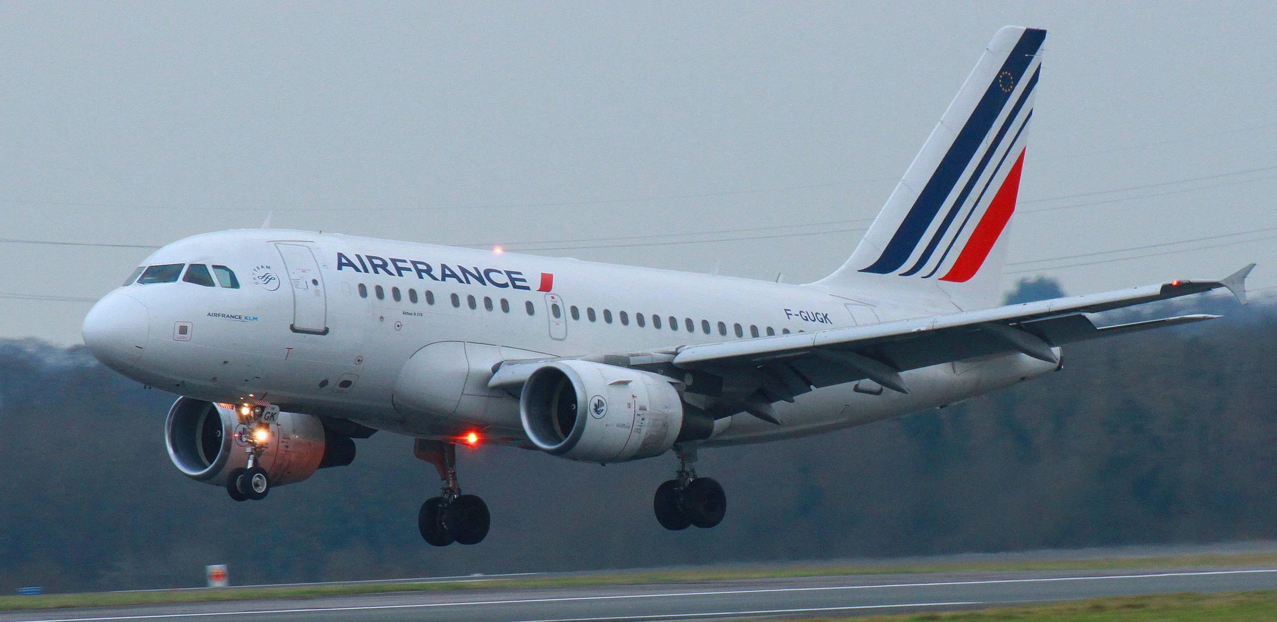 An Air France airplane in flight above the runway, with landing gear deployed, during cloudy weather.