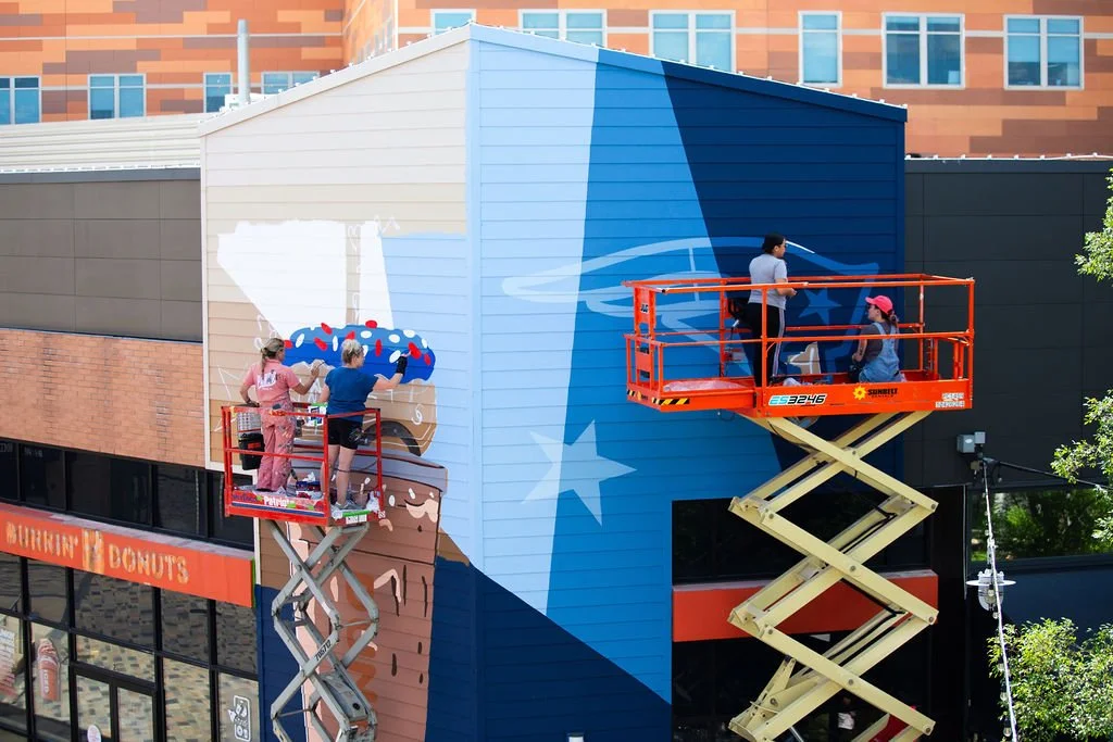 4 artists painting a Dunkin' x Patriots mural with blue and white paints.