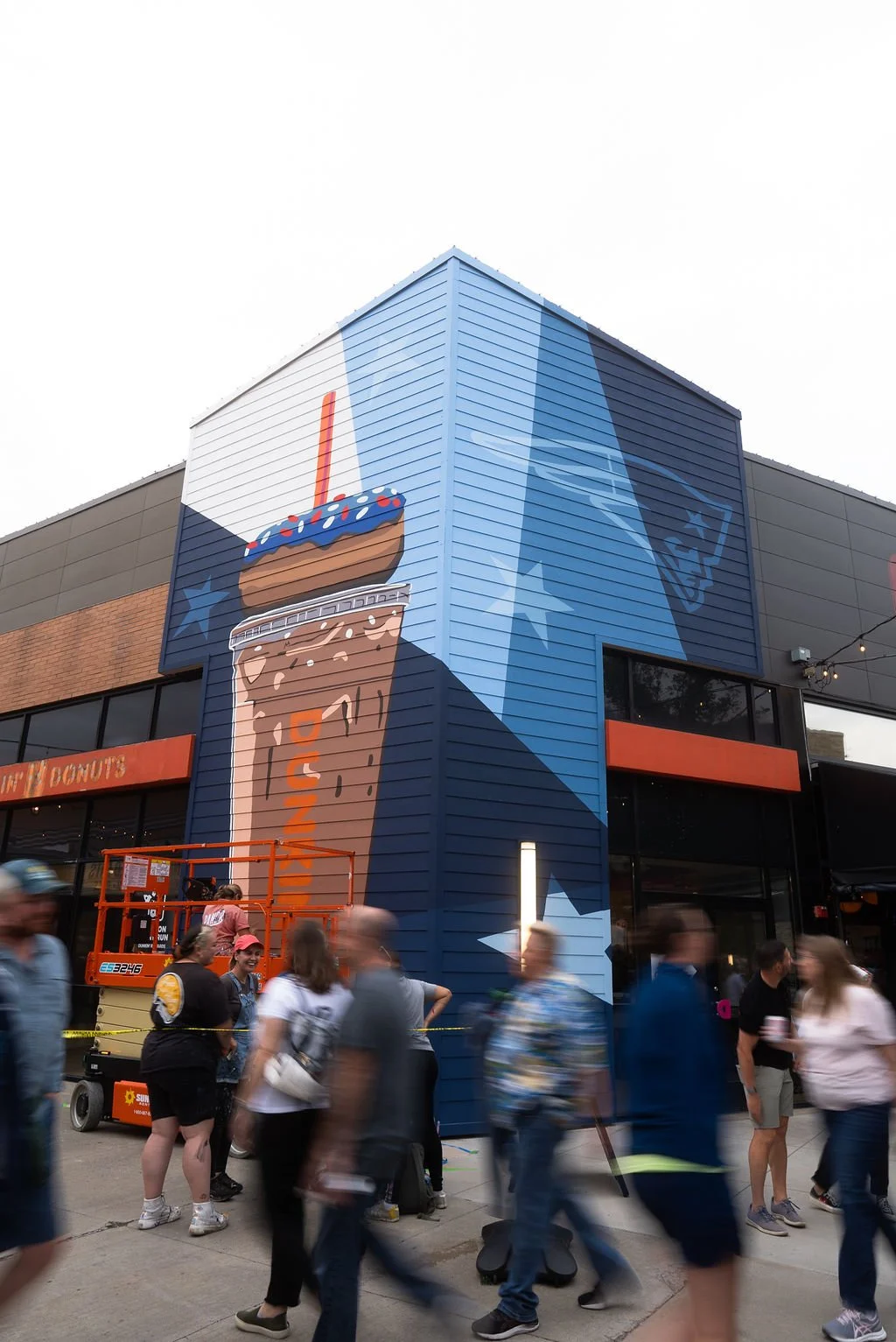 Exterior mural of a large Dunkin' drink, donut, and Patriots logo.
