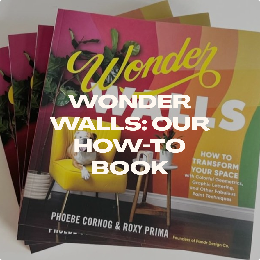 Book titled "Wonder Walls: Our How-To Book" by Phoebe Cornog and Roxy Prima, featuring a colorful wall with geometric shapes, a yellow chair with a dog sitting on it, and a side table with a toy.