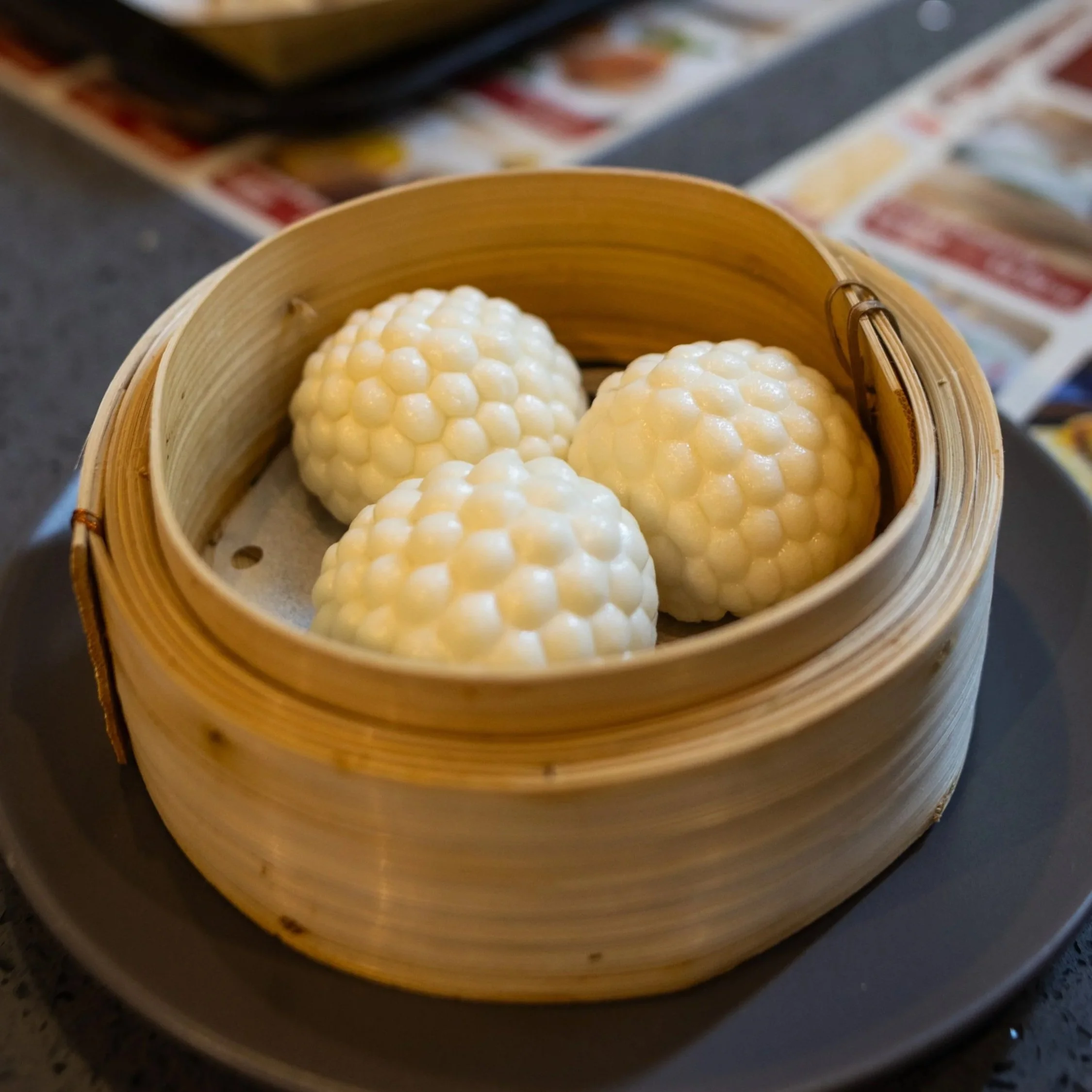 Three white cannabis buds inside a round bamboo steamer basket.