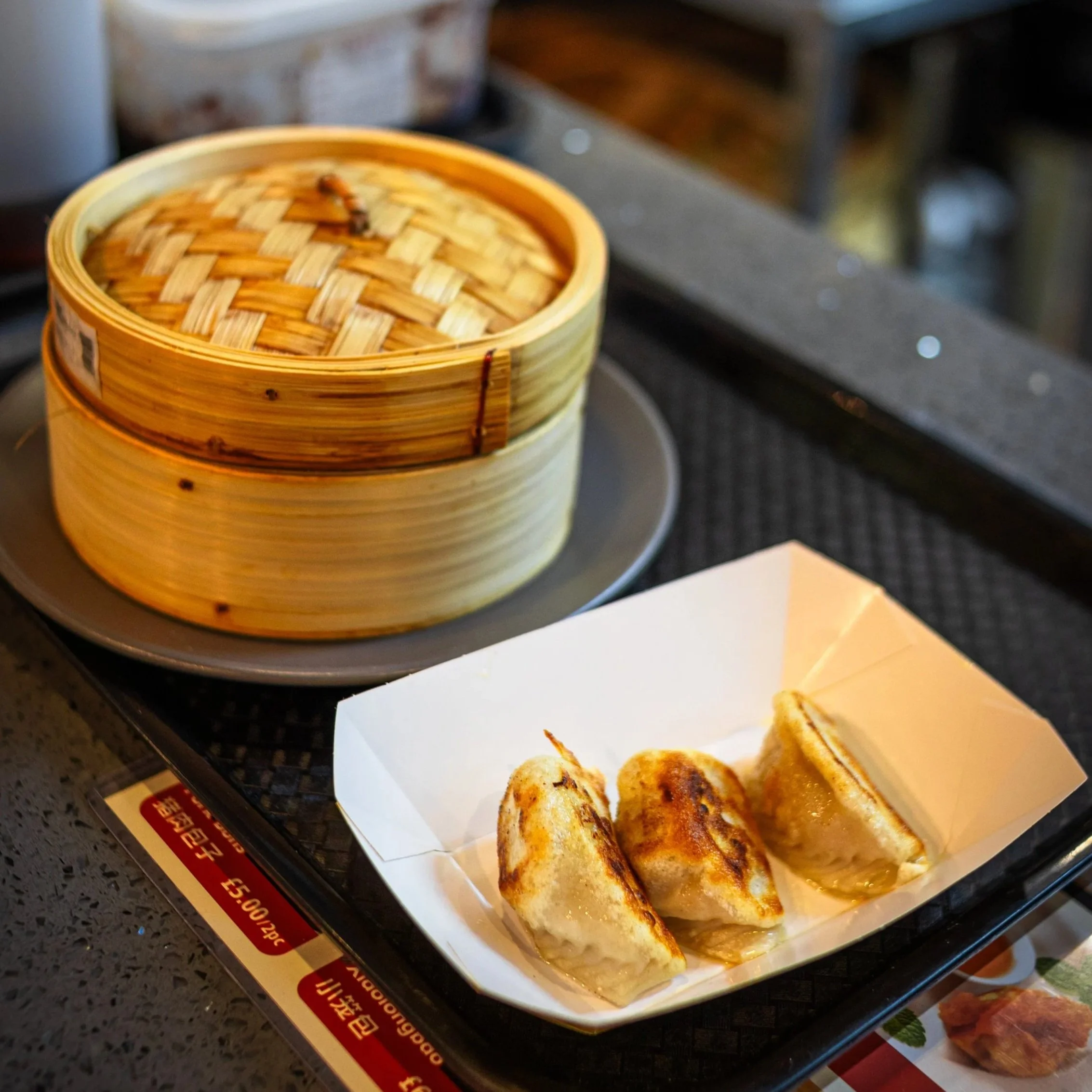 A bamboo steamer filled with dim sum, and three fried dumplings on a paper-lined tray.