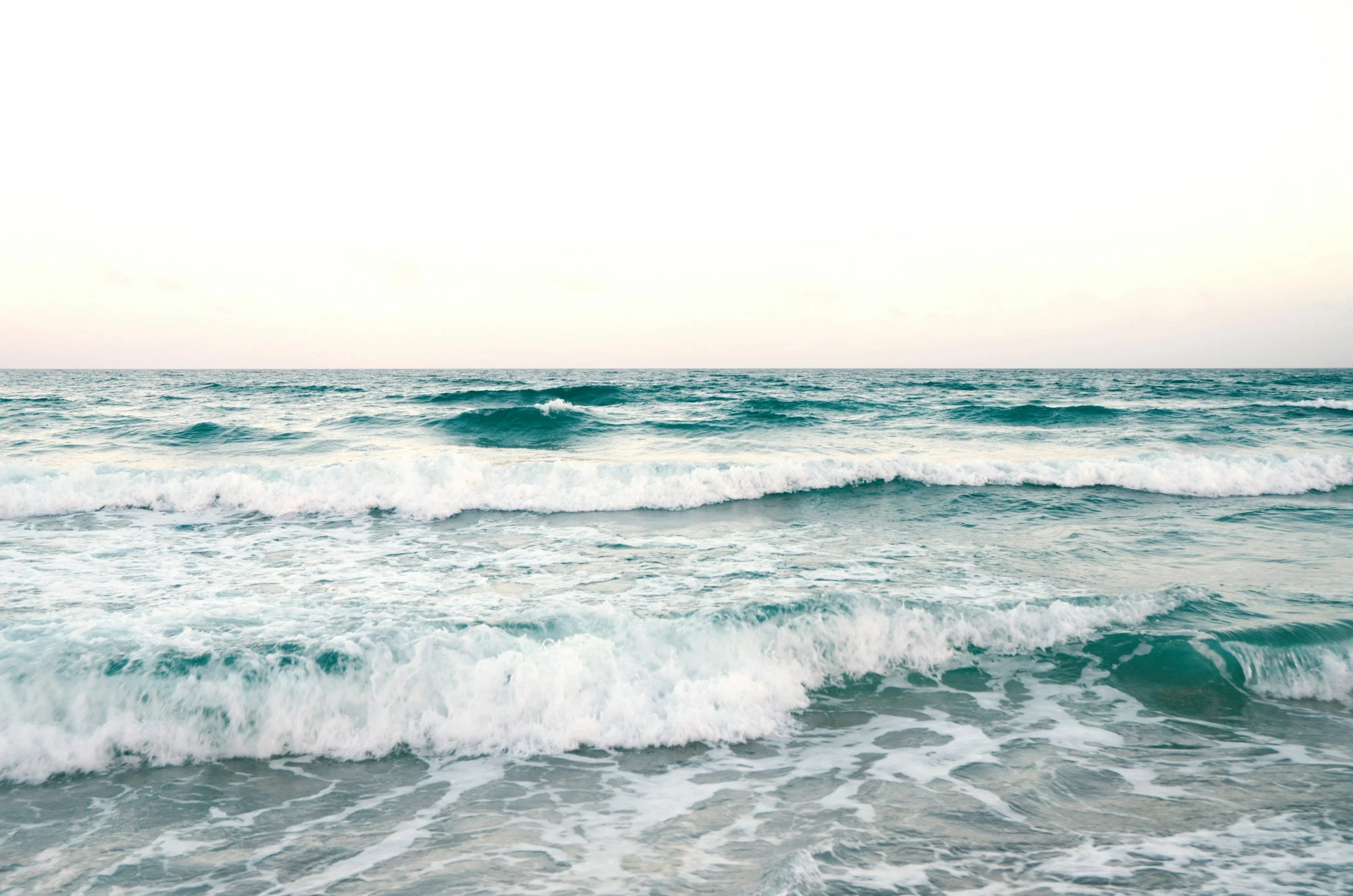 The image depicts the ocean with gentle waves and a light sky in the background.