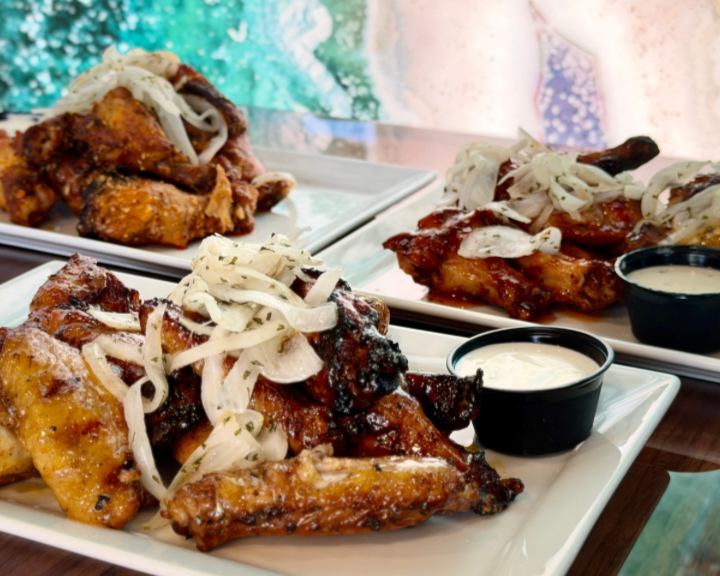 Three plates of chicken wings topped with shredded onions and served with small cups of dipping sauce.