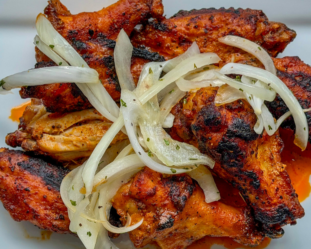 Close-up of grilled chicken pieces topped with sliced onions and herbs.