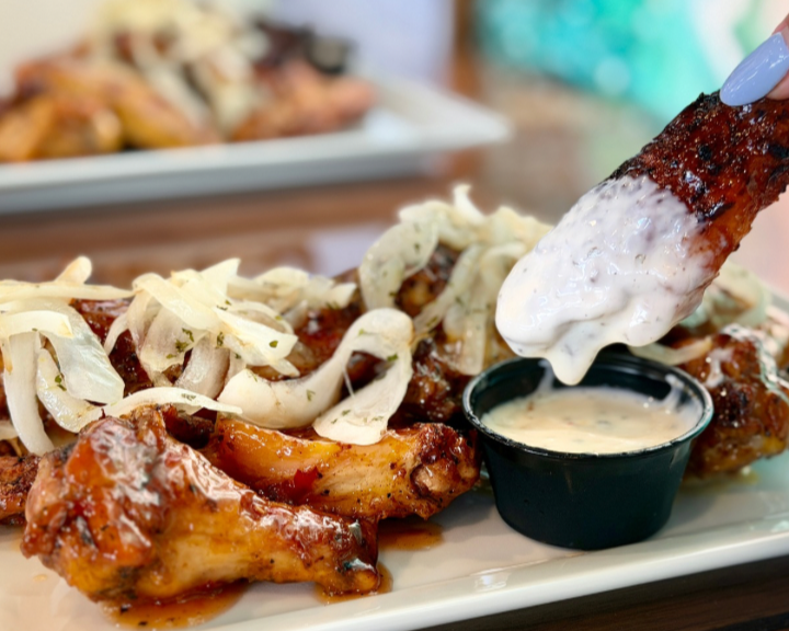 Barbecue chicken wings topped with shredded cheese and served with a side of creamy dipping sauce.