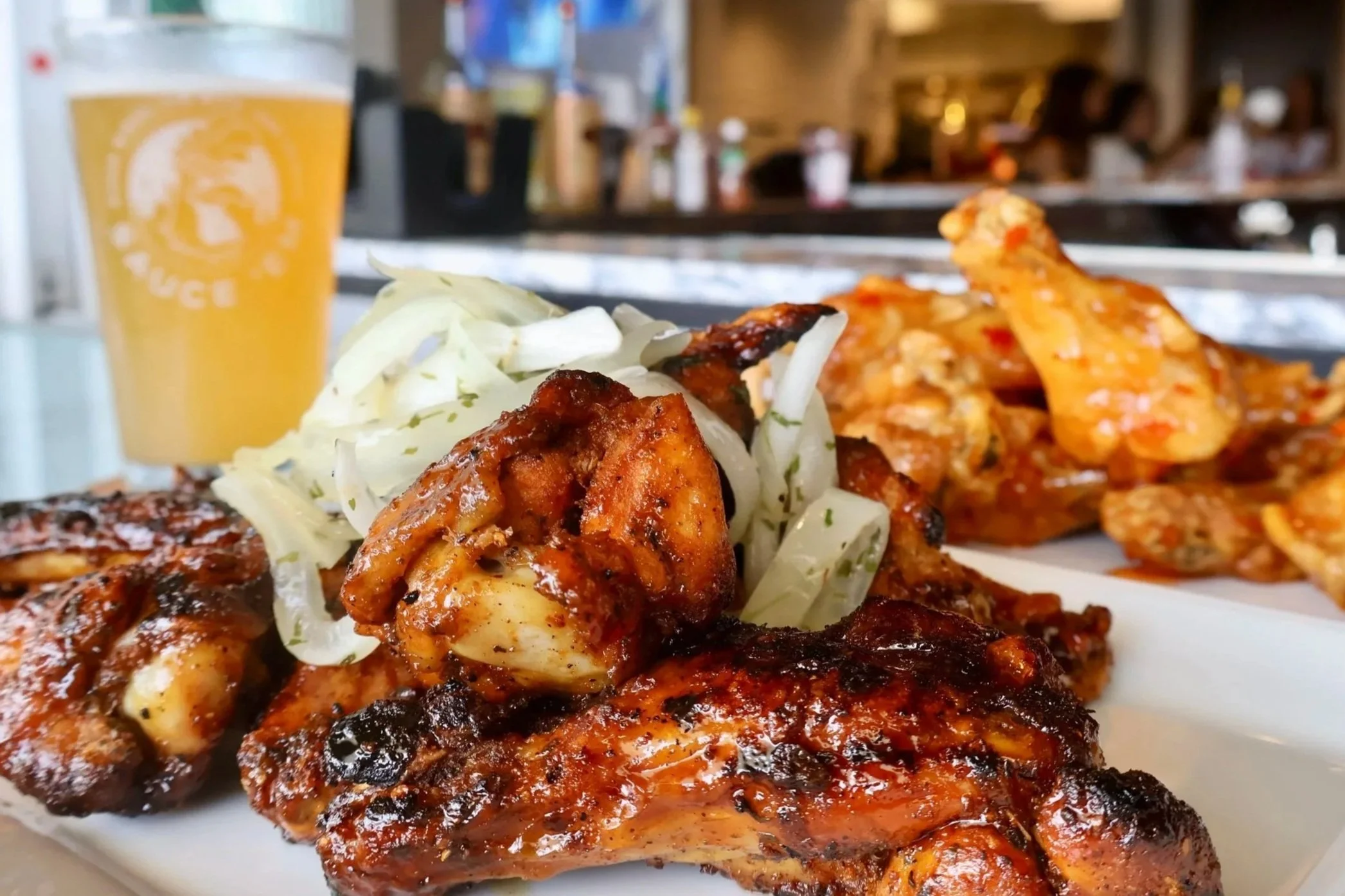 Close-up of grilled chicken with barbecue sauce, served with sliced onions and a glass of beer in a restaurant.
