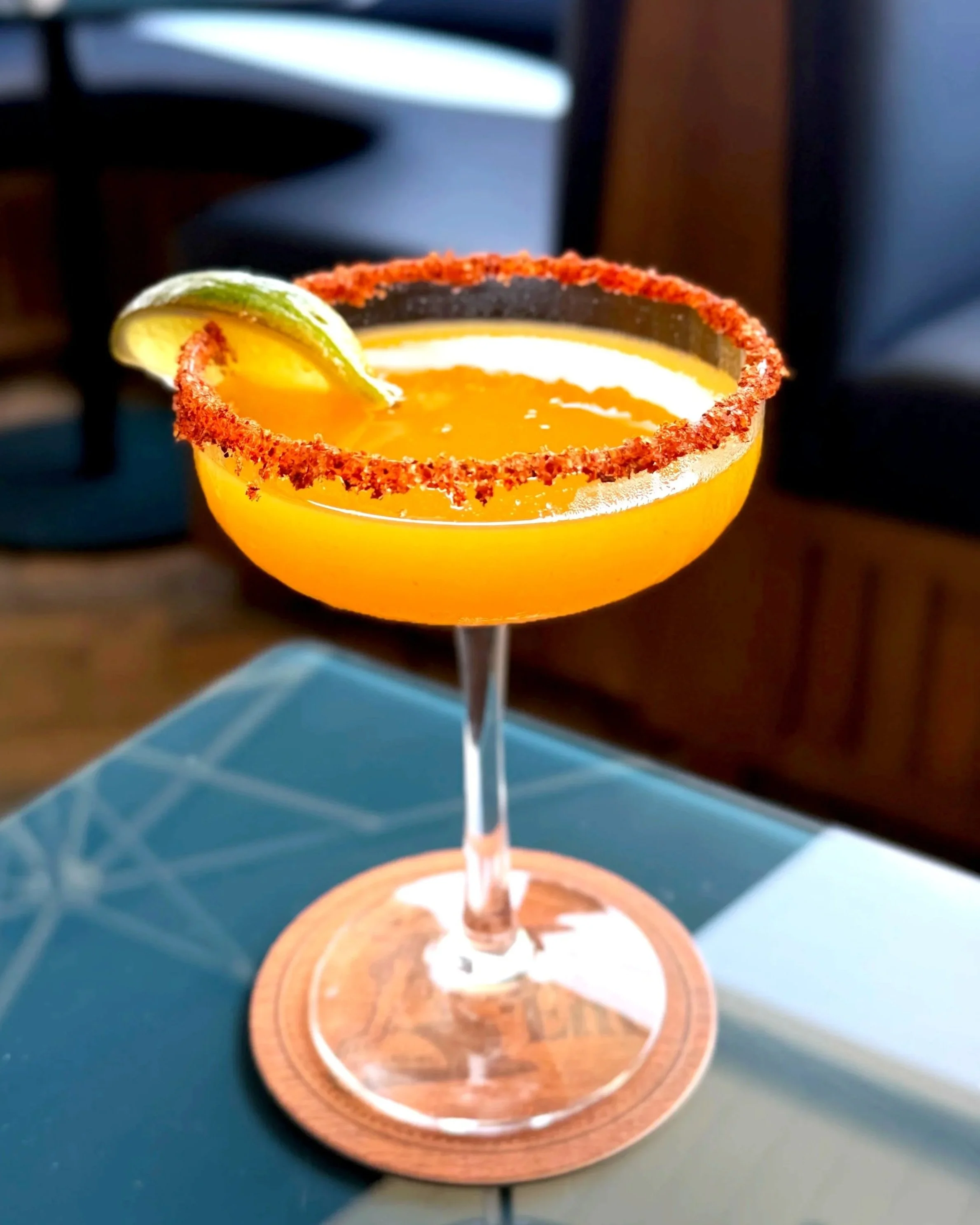 A colorful margarita cocktail in a glass with salted rim, garnished with a lime wedge, on a wooden coaster.