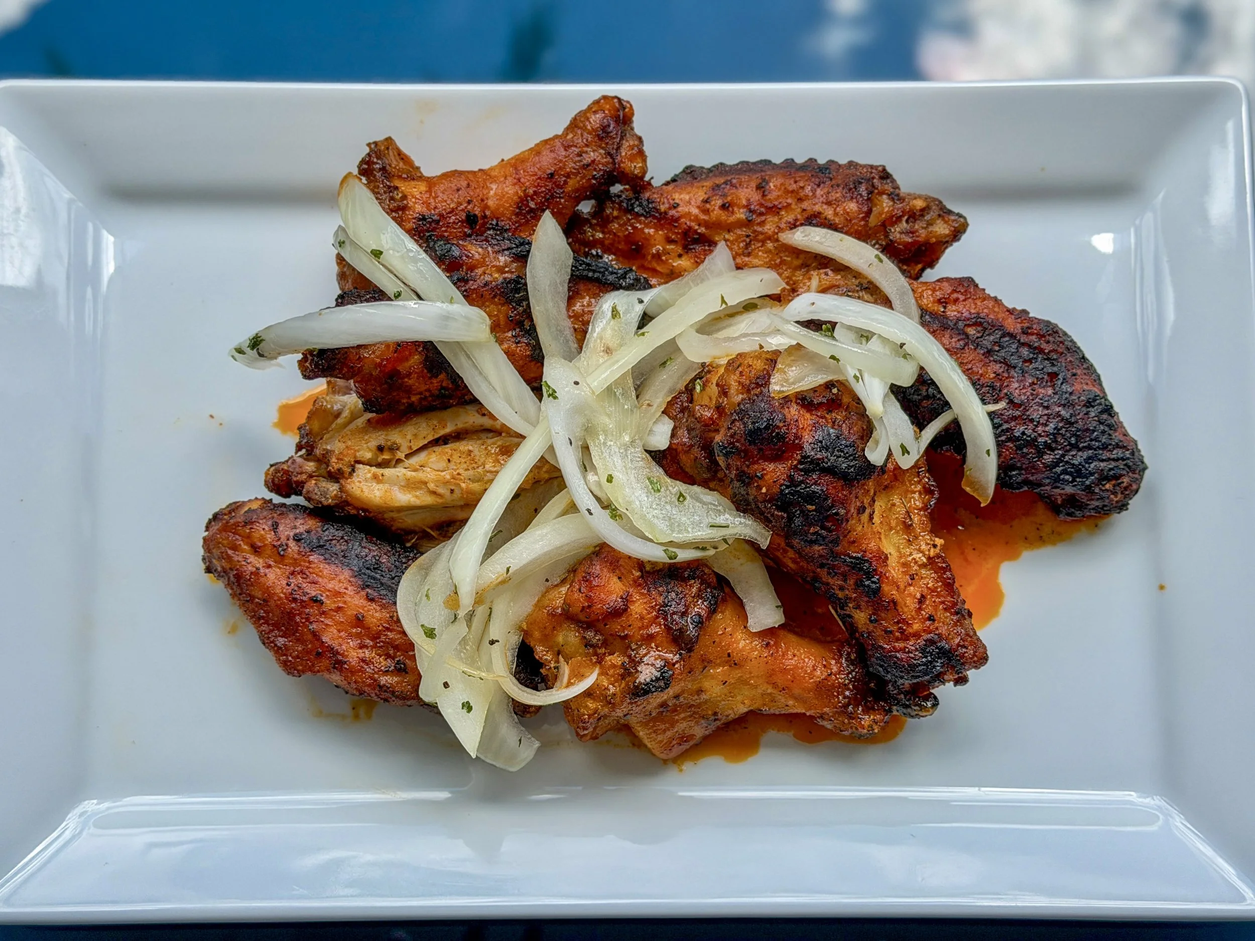 Grilled chicken with some char marks topped with sliced onions on a white rectangular plate.