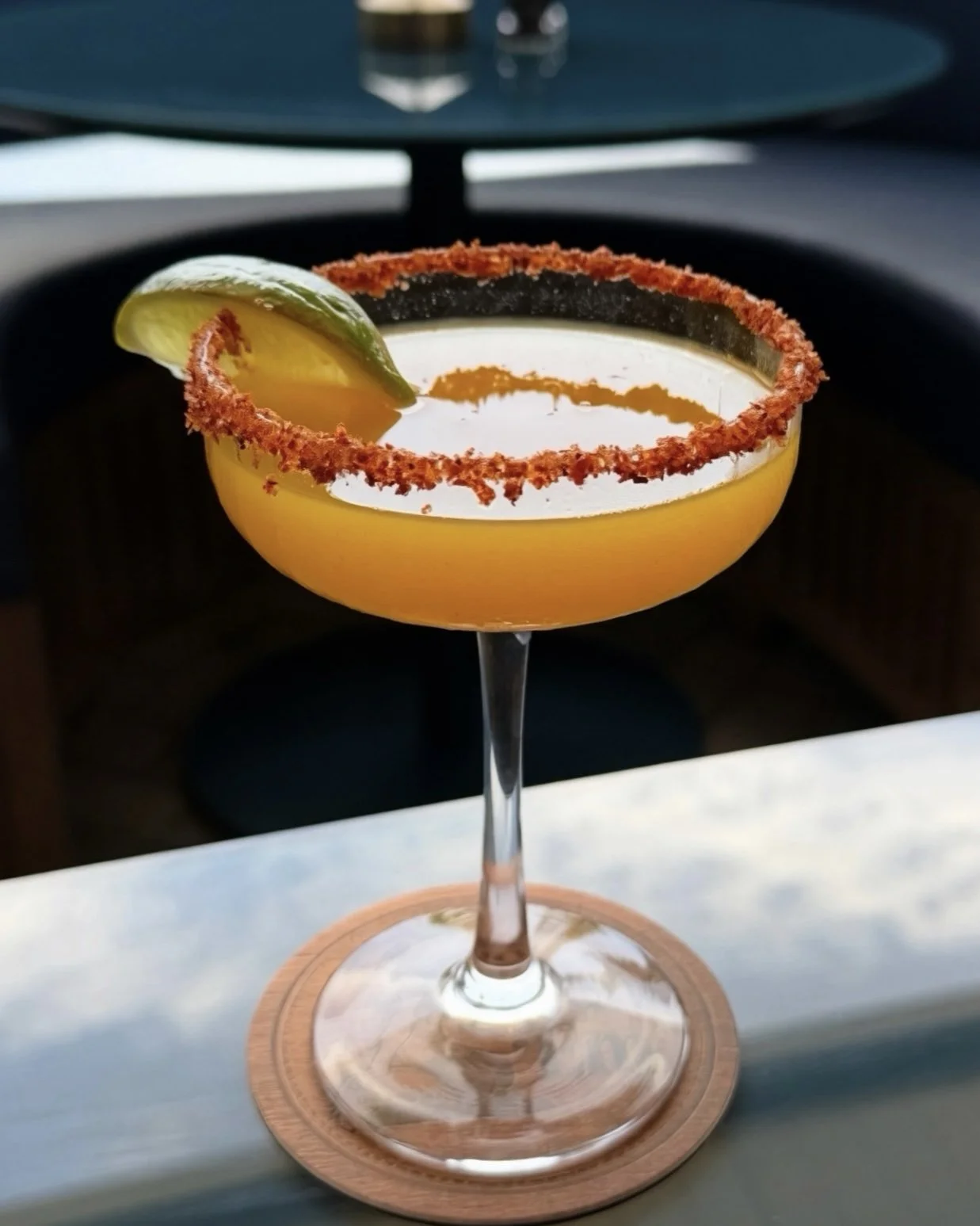 A margarita cocktail in a stemmed glass with a salted rim and a lime wedge garnish, placed on a wooden coaster.