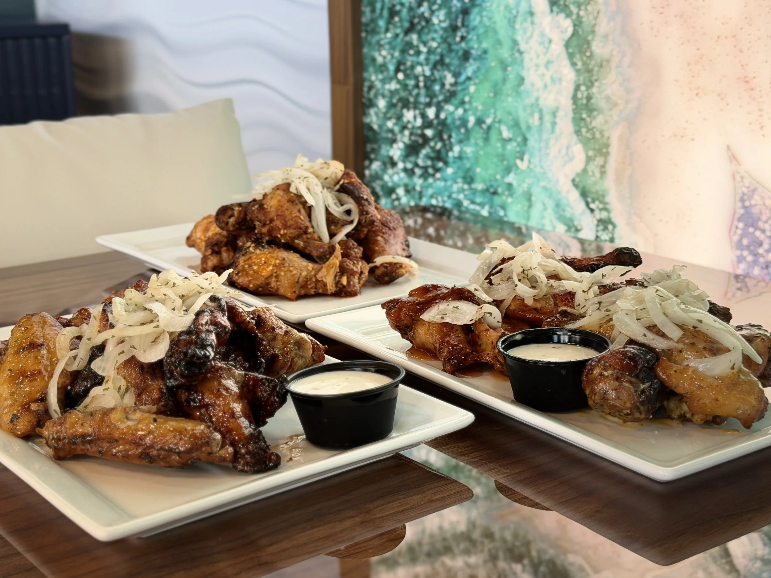 Plate of assorted grilled chicken wings topped with onions and served with dipping sauces on a table.