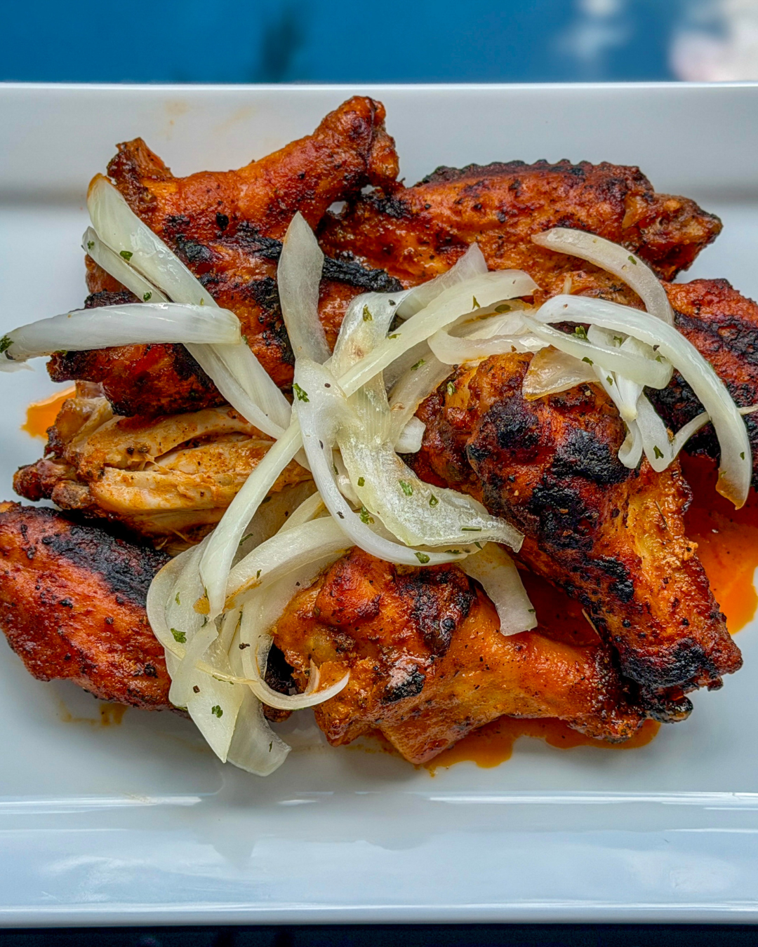 Grilled chicken pieces topped with sliced onions on a white plate.
