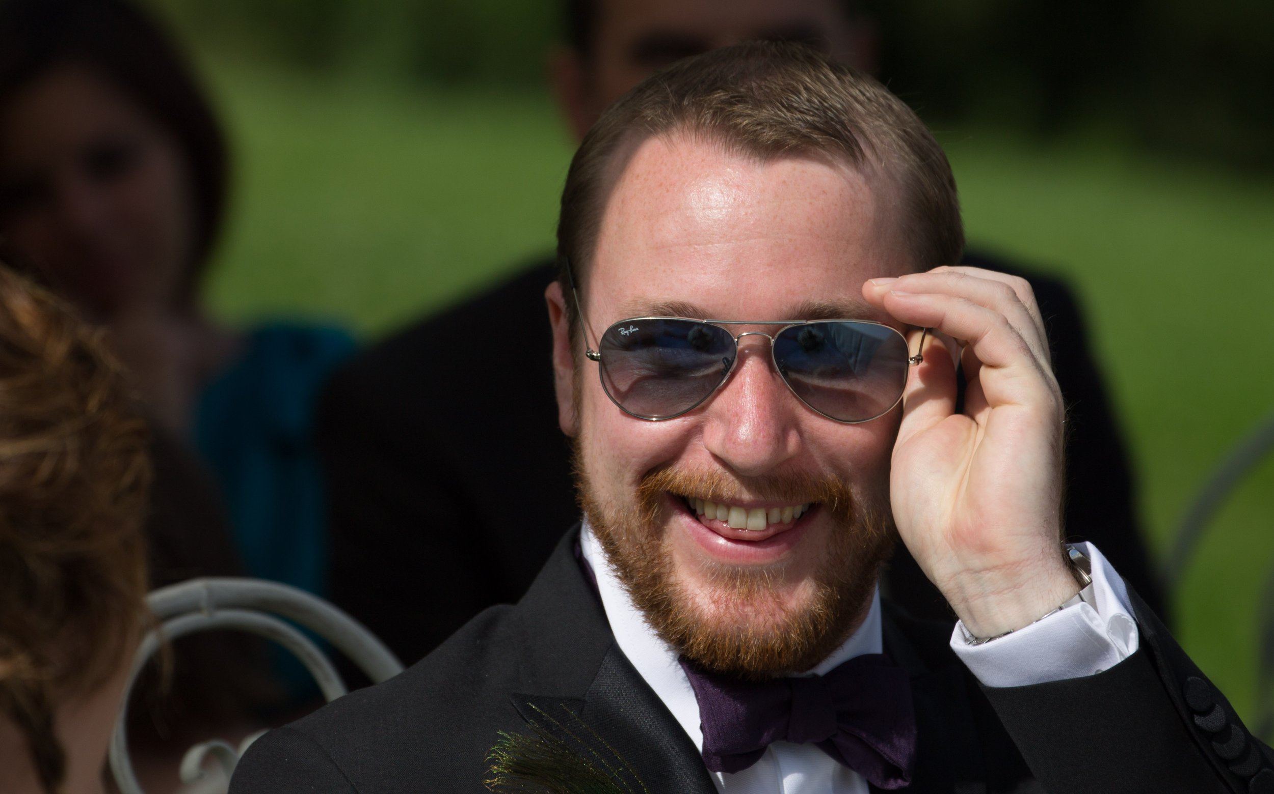 Ein lachender Mann mit Brille, im Anzug, bei einer sozialen Veranstaltung im Freien.