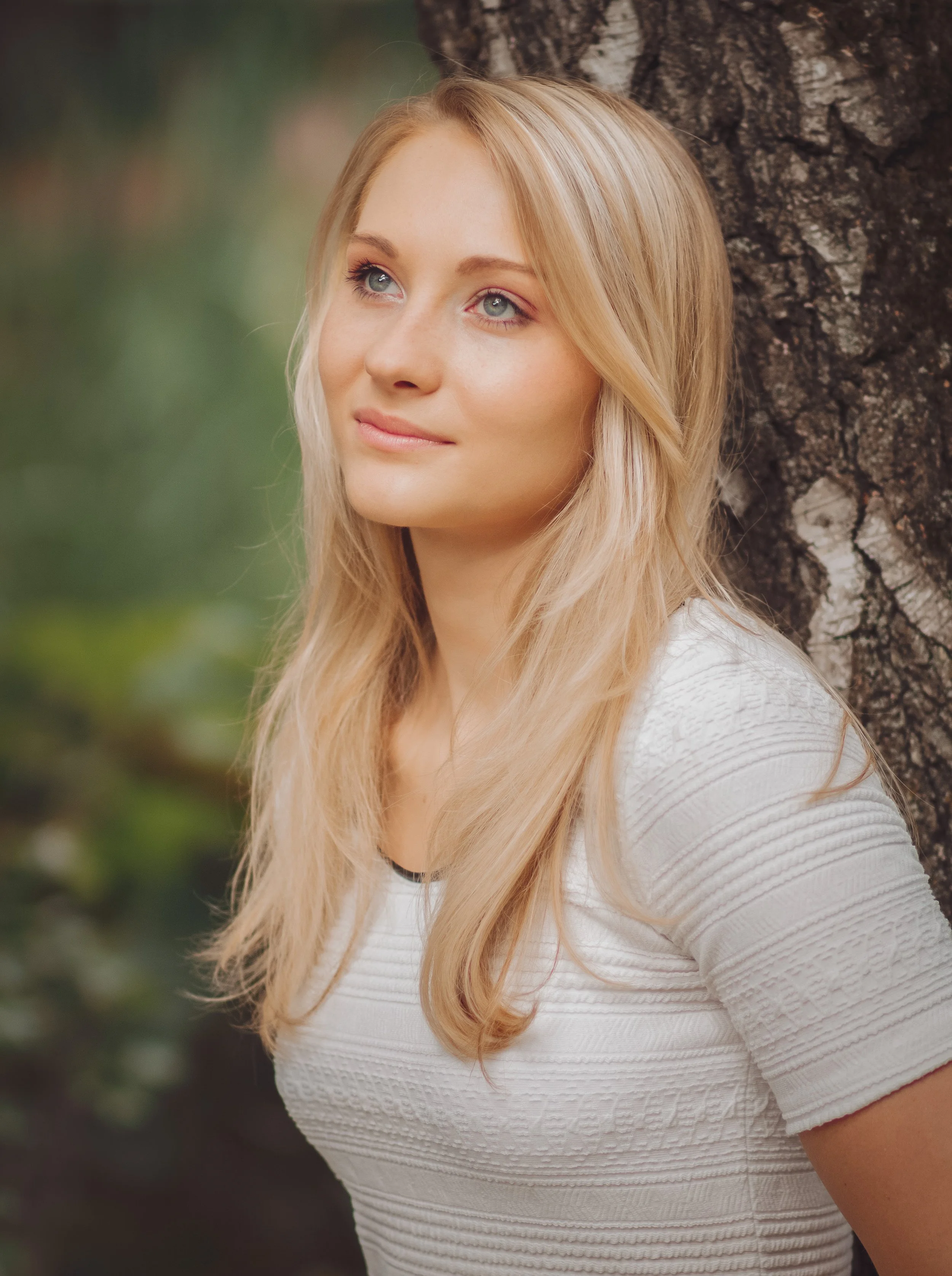 Junge Frau mit blonden, lockigen Haaren, die an einem Baum im Freien steht.