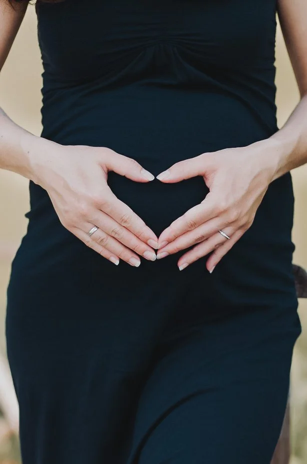 Eine schwangere Person hält Hände in Herzform vor den Bauch.