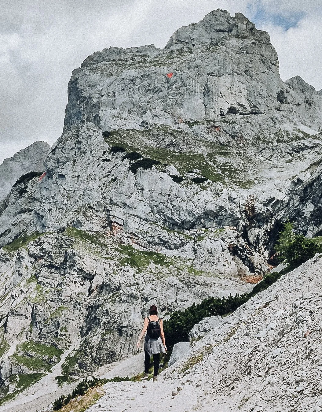 Eine Person wandert auf einem schmalen Weg in den Bergen, umgeben von riesigen Felsen und Bergen im Hintergrund.