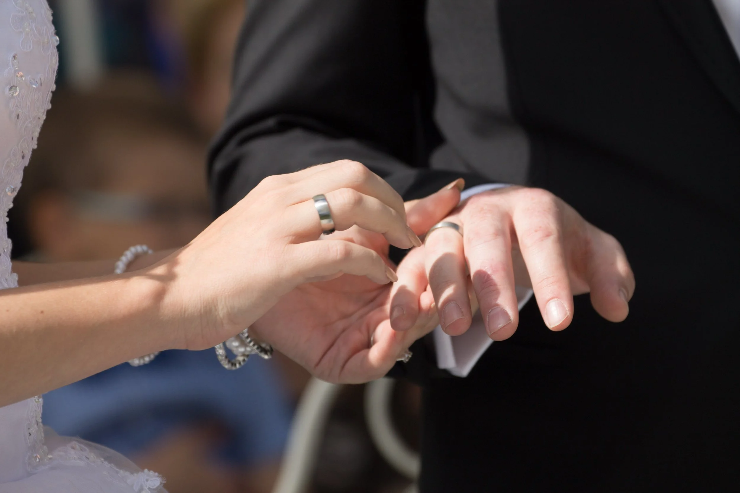 Ein Hochzeitsring wird an den Ringfinger einer Frau gesetzt, während die Hand eines Mannes hält.