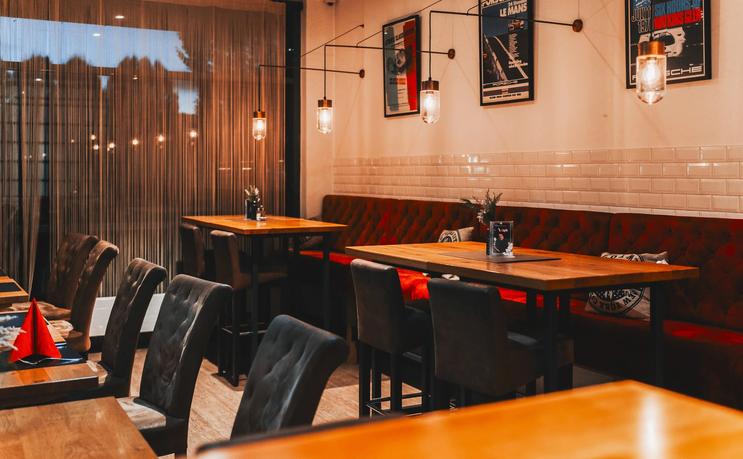 Innenraum eines Restaurants mit Holztischen, schwarzen Stühlen, Wanddekorationen und hanging Lampen, warme Beleuchtung, Poster an der Wand.