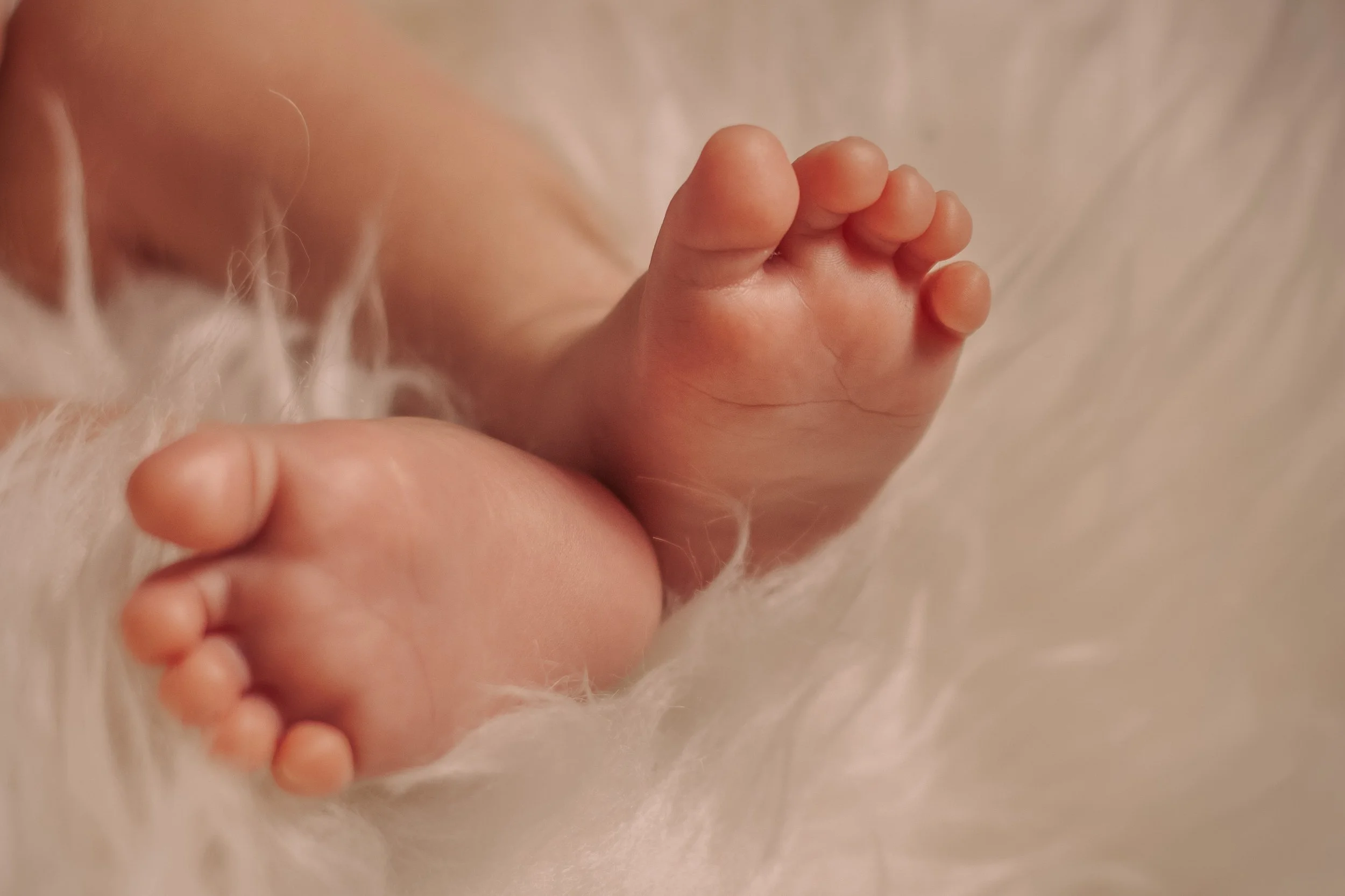 Nahaufnahme eines Babys mit Zehen, vor einem weichen, hellen Hintergrund.