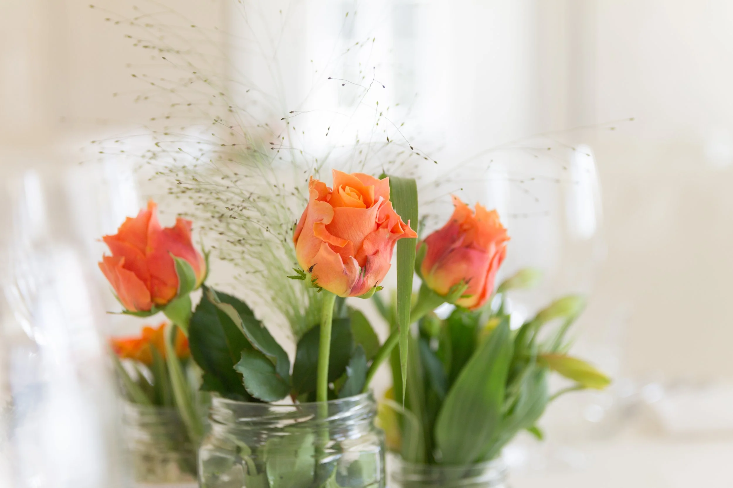 Bunter Blumenstrauß mit orangefarbenen Rosen in einer Vase auf einem Tisch, im Hintergrund unscharfer Raum mit natürlichem Licht.