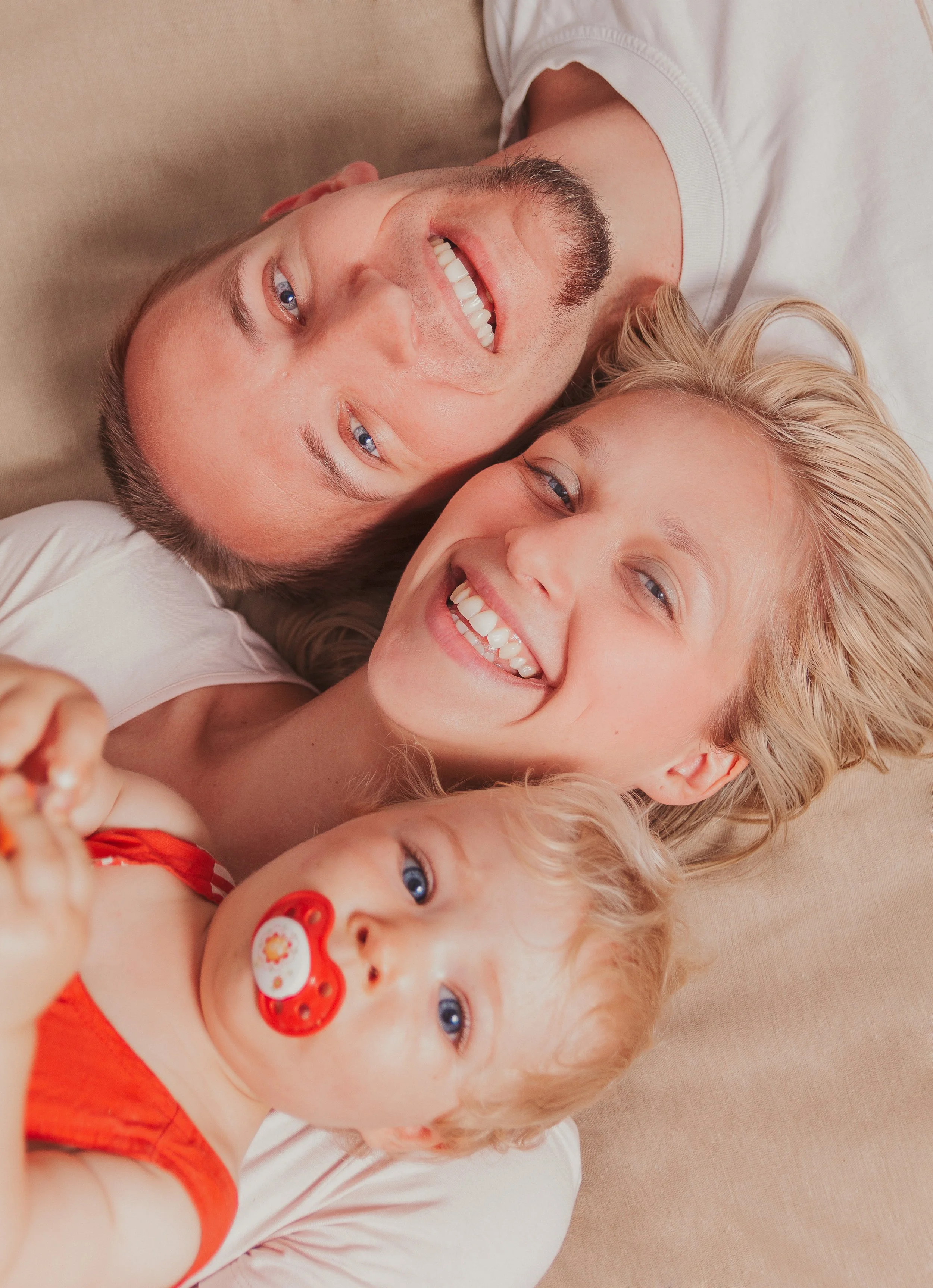 Vier Menschen, ein Mann, eine Frau und zwei Kinder, liegen eng nebeneinander auf einem Bett, lachen und schauen in die Kamera.