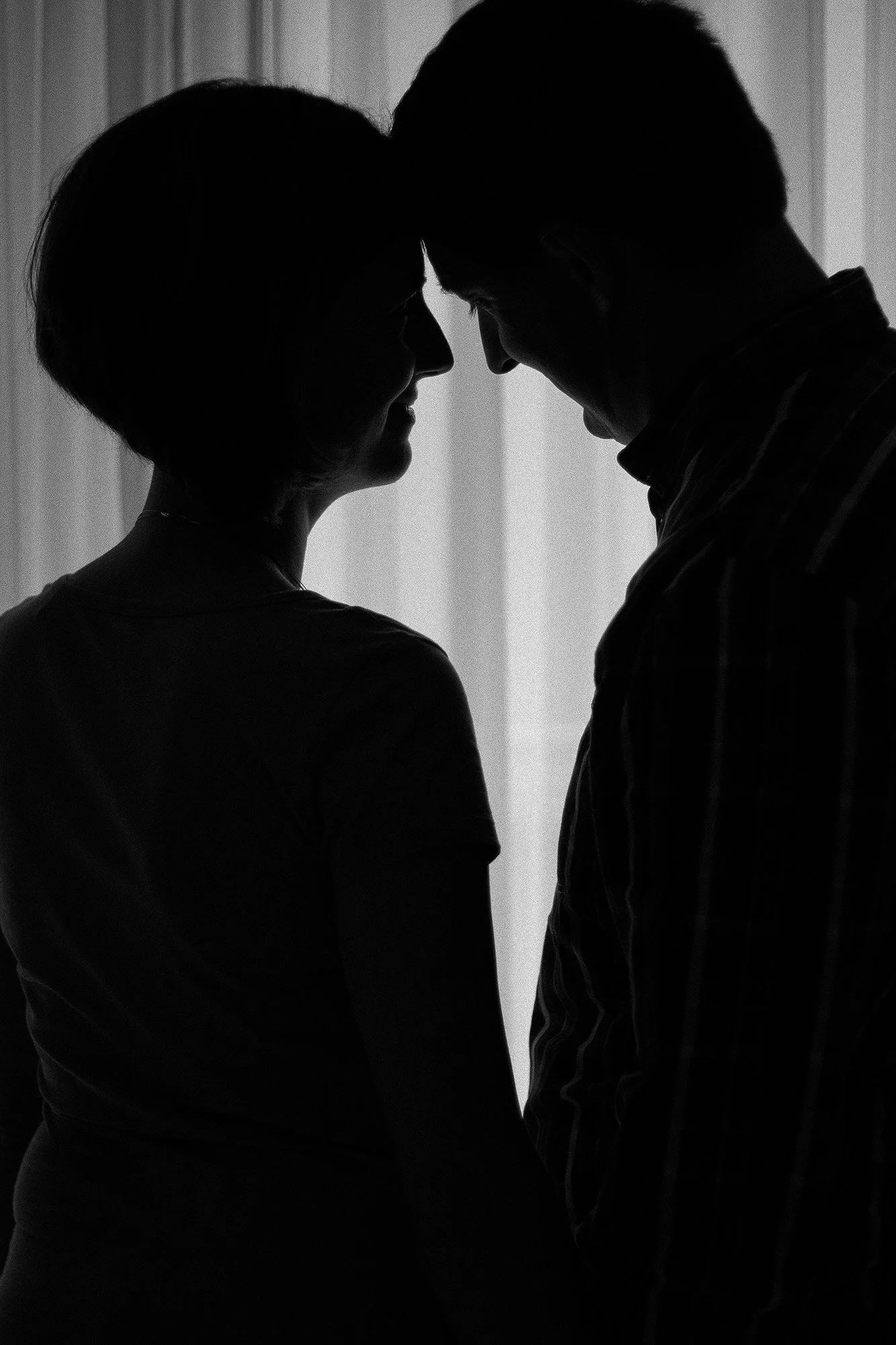 Zwei Menschen stehen sich gegenüber, ihre Stirn berühren sich, in einem schwarzen und weißen Bild, Silhouetten bei Kerzenschein.