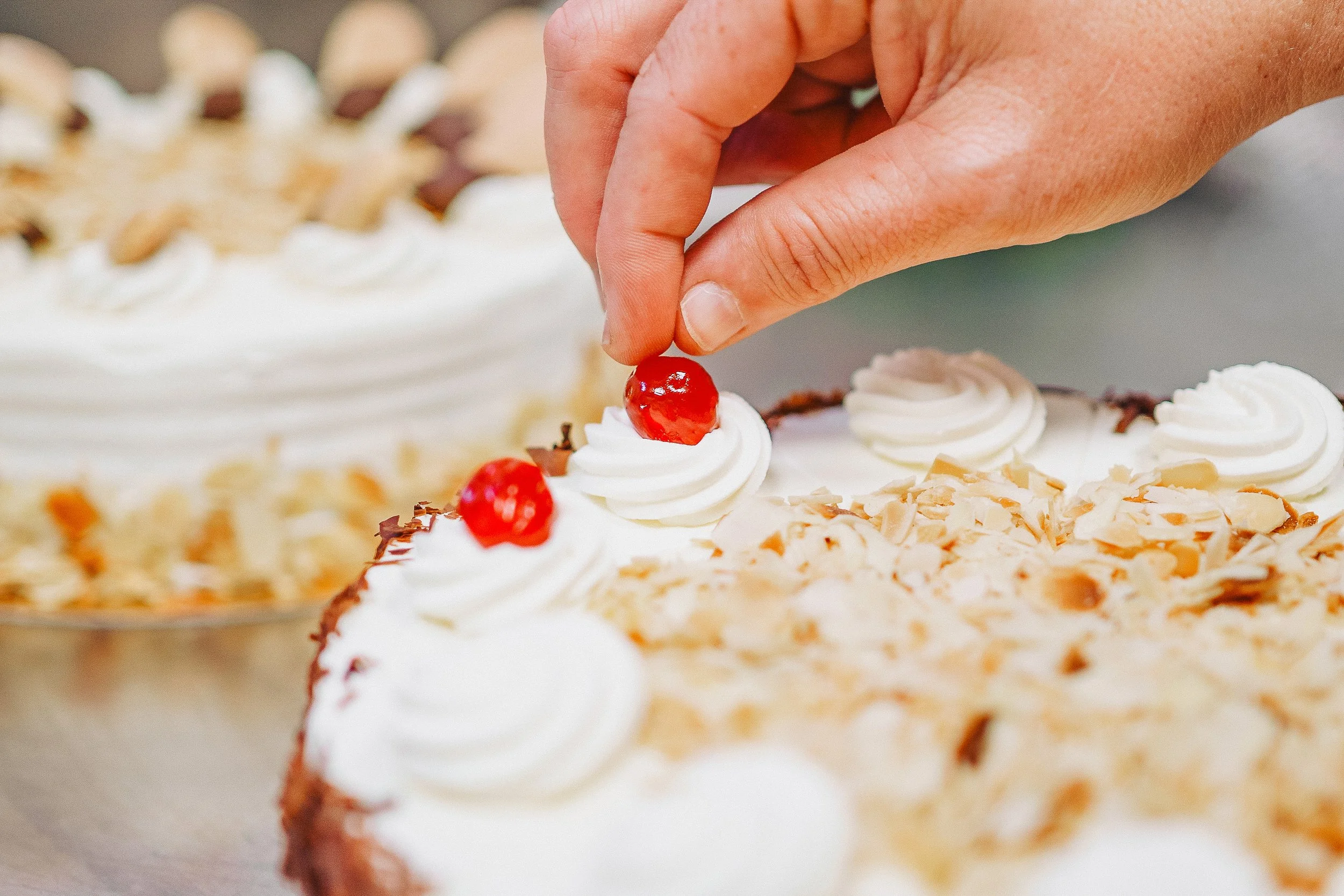 Hand, die eine Kirsche auf ein Stück Torte mit weißer Creme und Schokoladenstücken legt.