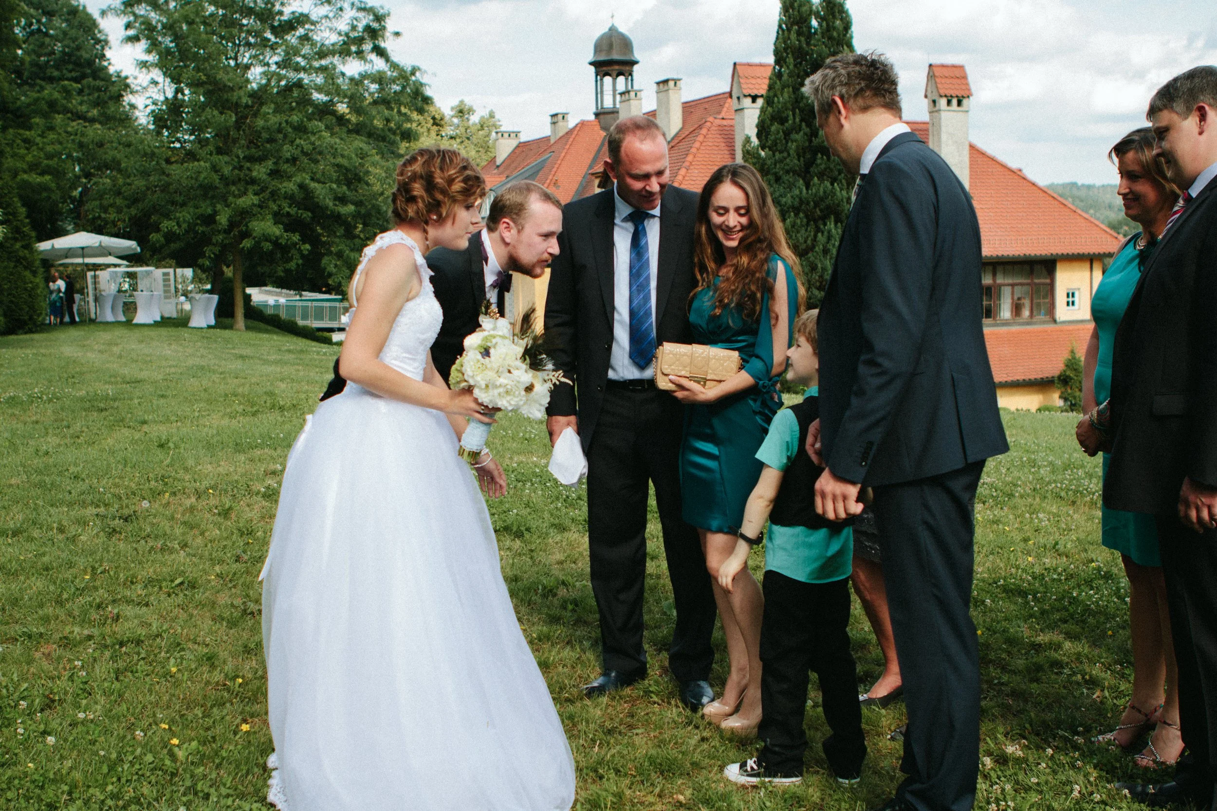 Hochzeit im Freien mit Braut, Bräutigam und Gästen, die im Garten stehen und sich unterhalten.