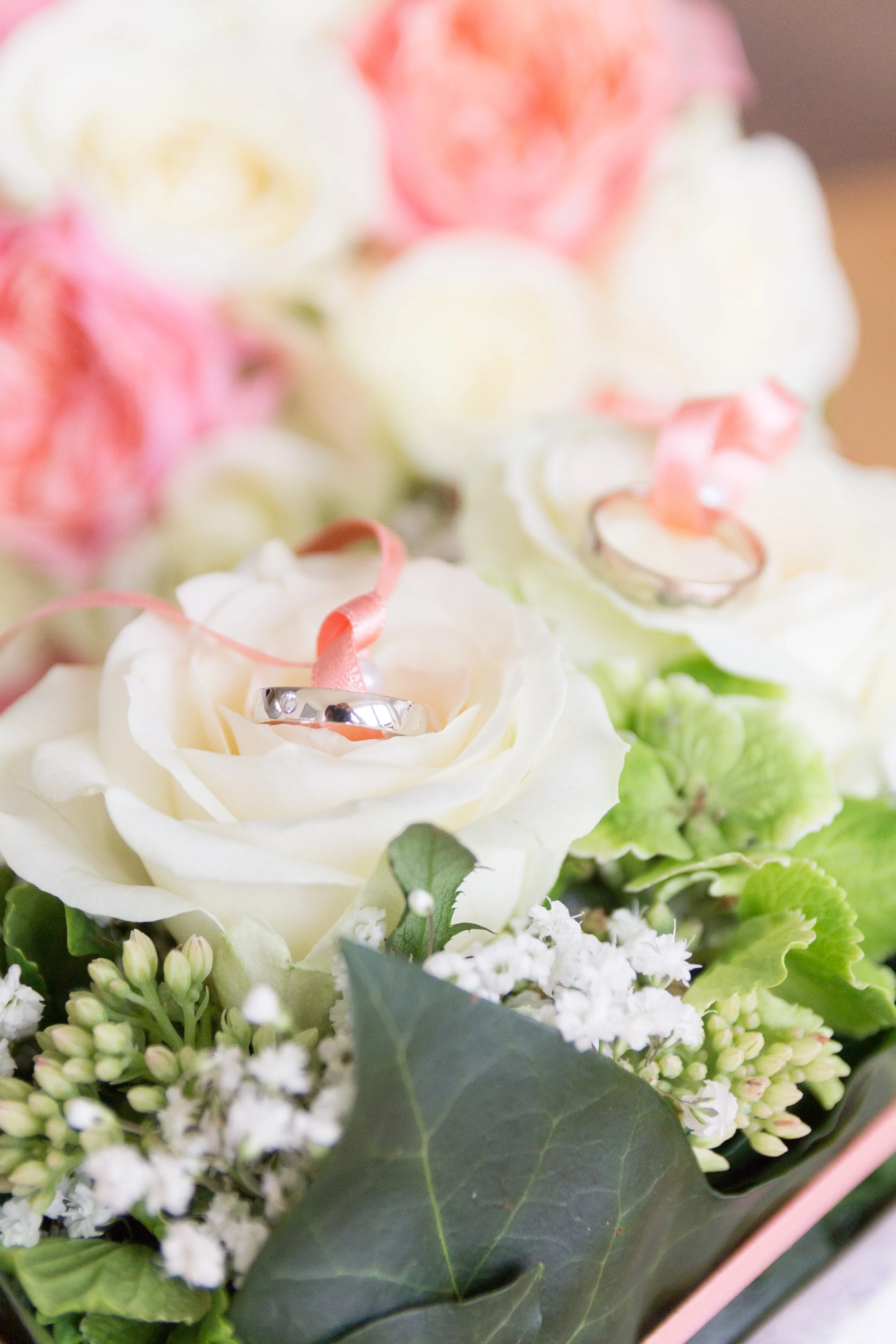 Ein Blumenstrauß mit weißen Rosen, kleinen weißen Blüten, grünen Blättern und Ring auf einer weißen Rose.