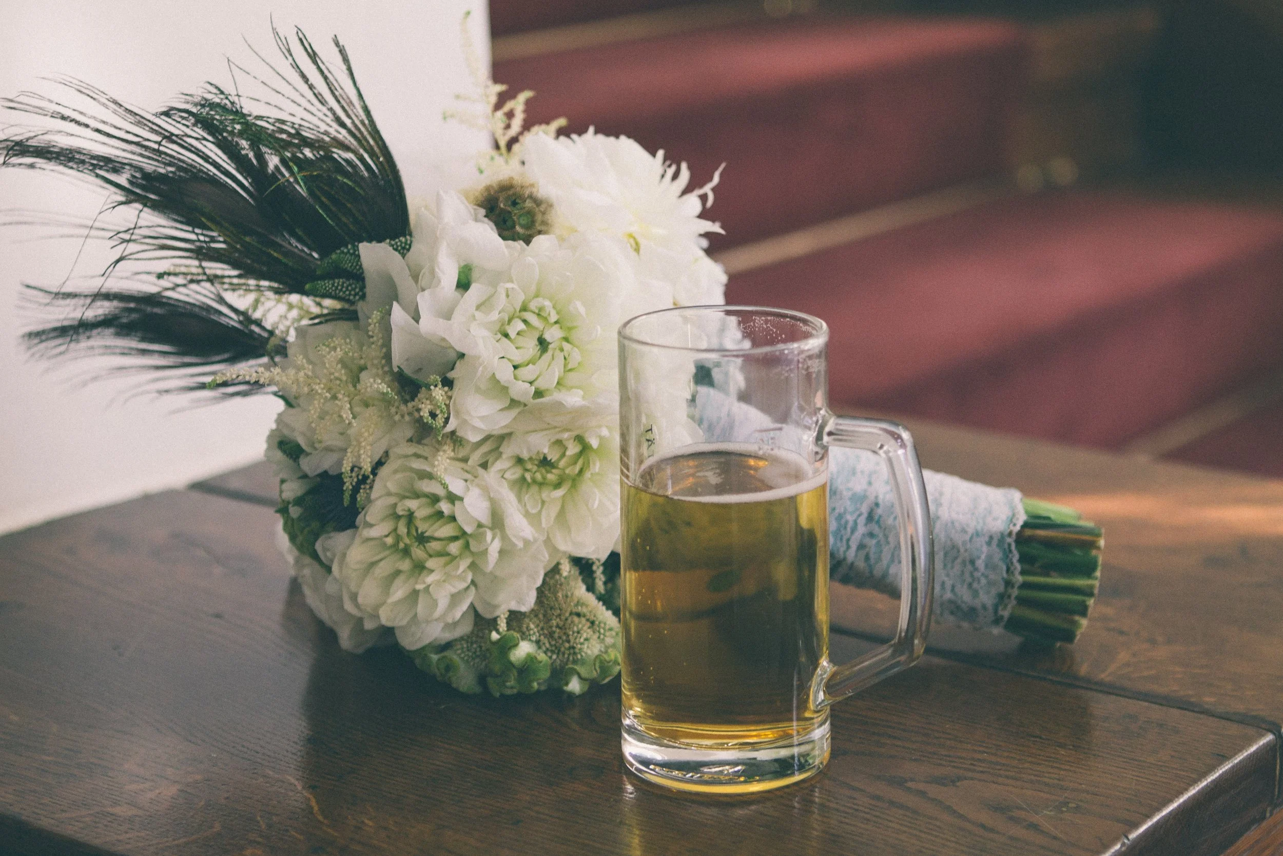 Ein Glas Bier neben einem Blumenbouquet auf einem Holztisch.