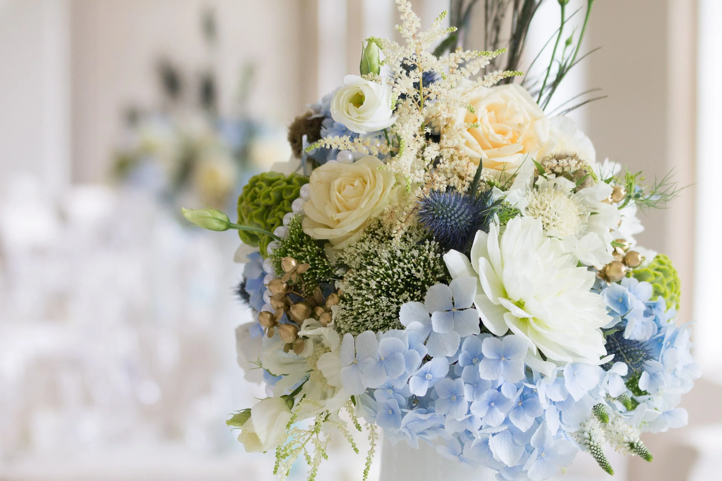 Blumenstrauß mit weißen Rosen, blauen Hortensien und anderen weißen und grünen Blumen auf einem Tisch.