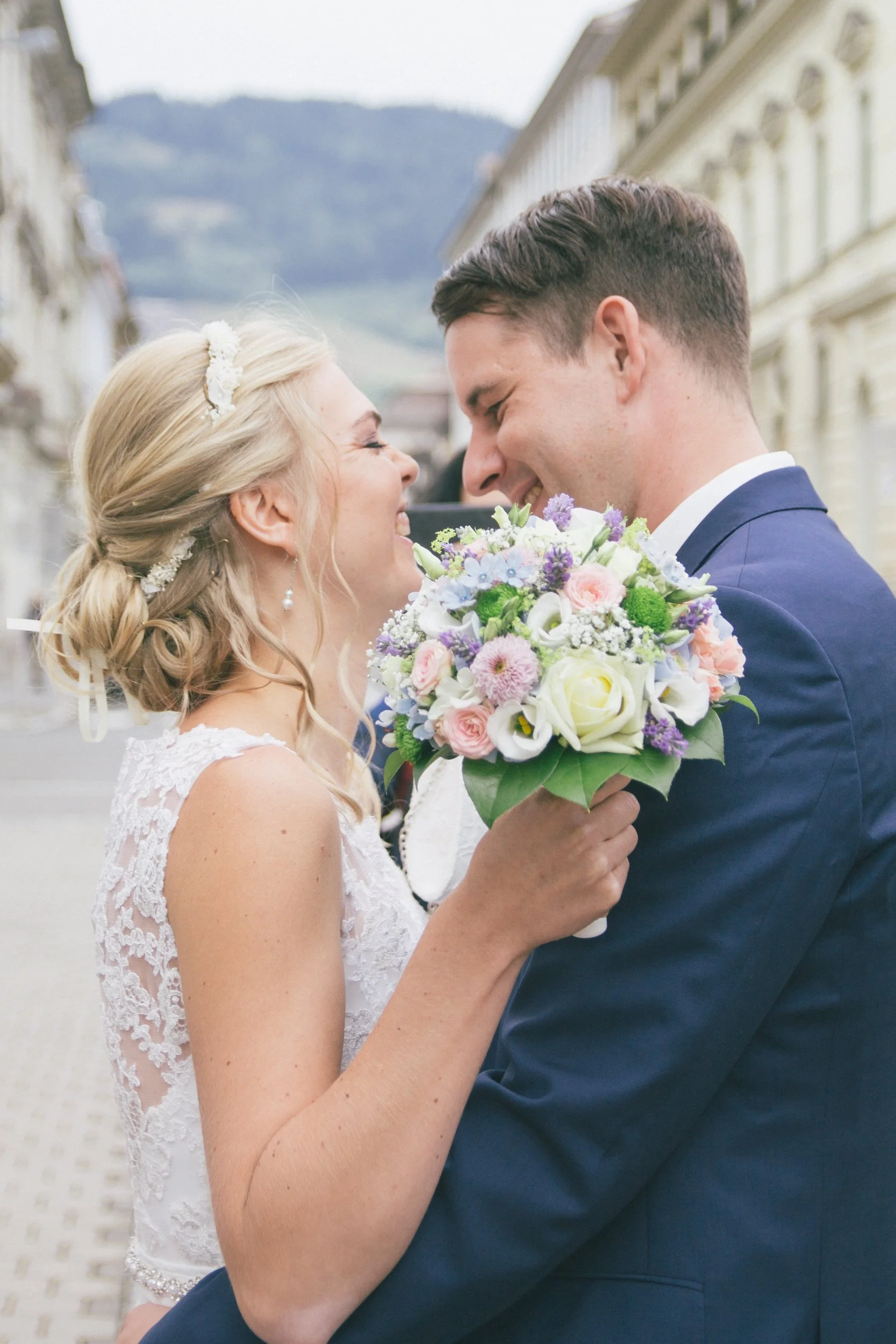 Braut und Bräutigam stehen sich bei ihrer Hochzeit gegenüber, lächeln und halten sich an den Händen, mit einer Blumenstrauß.