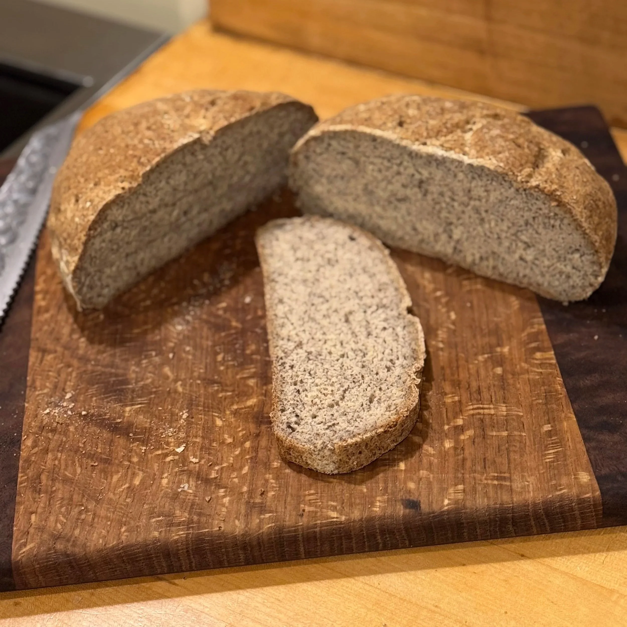 Round loaf of homemade bread with a cross cut on top, resting on a dark wooden cutting board.