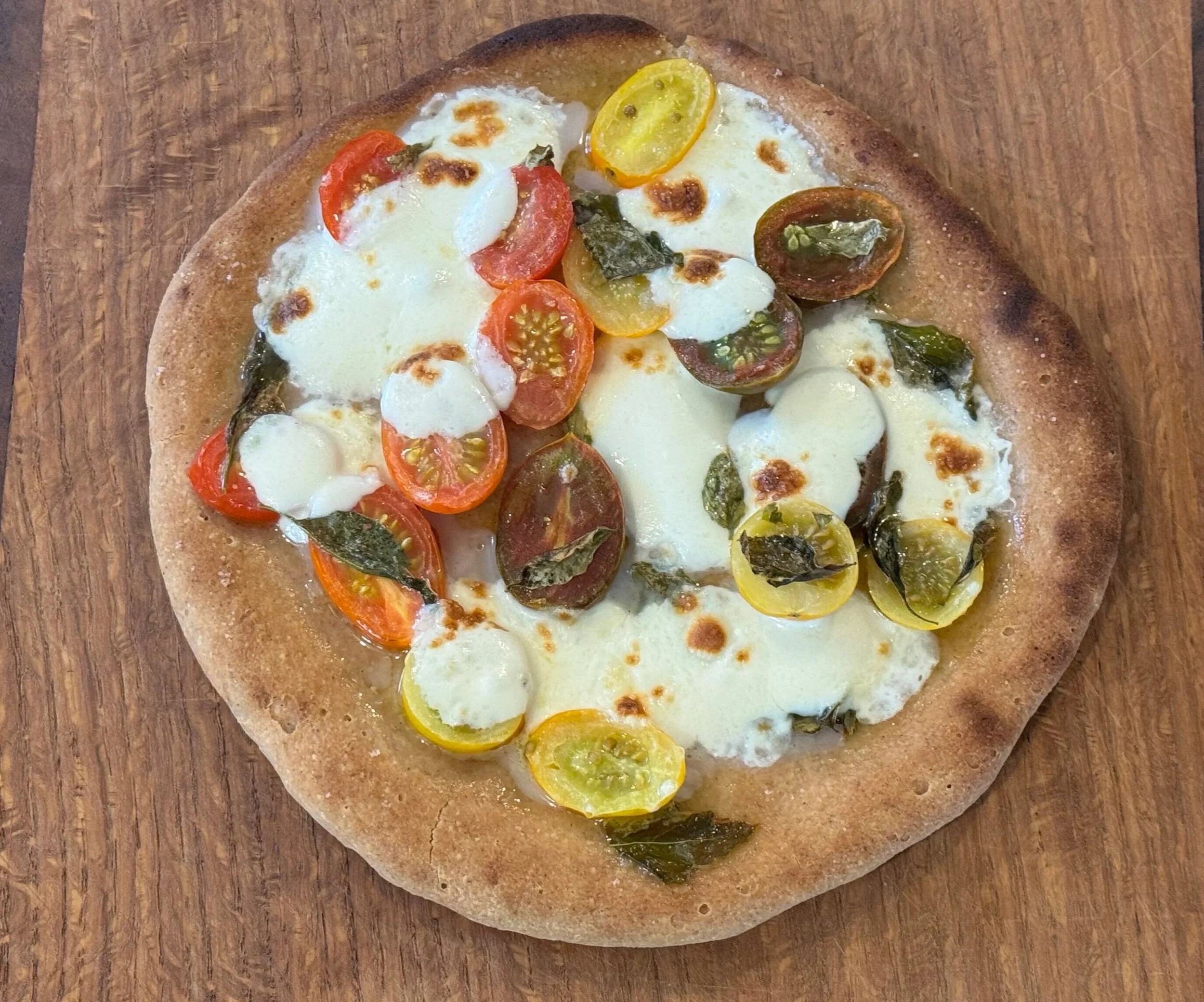 Personal pizza with cherry tomatoes, mozzarella cheese, and basil leaves on a wooden surface.