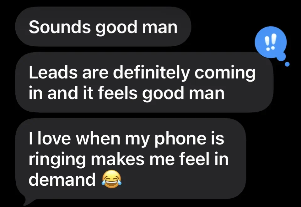 A digital chat message conversation in black speech bubbles. The messages say "Sounds good man", "Leads are definitely coming in and it feels good man", and "I love when my phone is ringing makes me feel in demand" with a laughing emoji at the end. There is a blue exclamation mark icon next to the messages.
