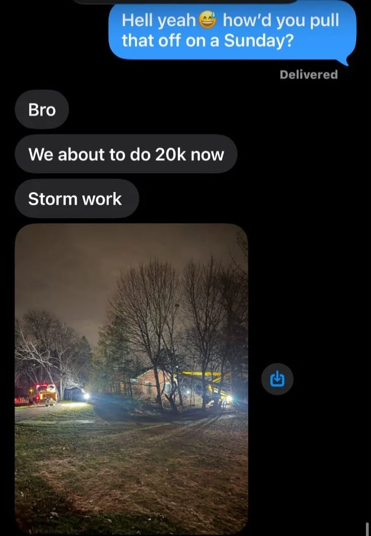 Nighttime scene showing a damaged house with fallen trees, emergency vehicles, and storm aftermath lights.