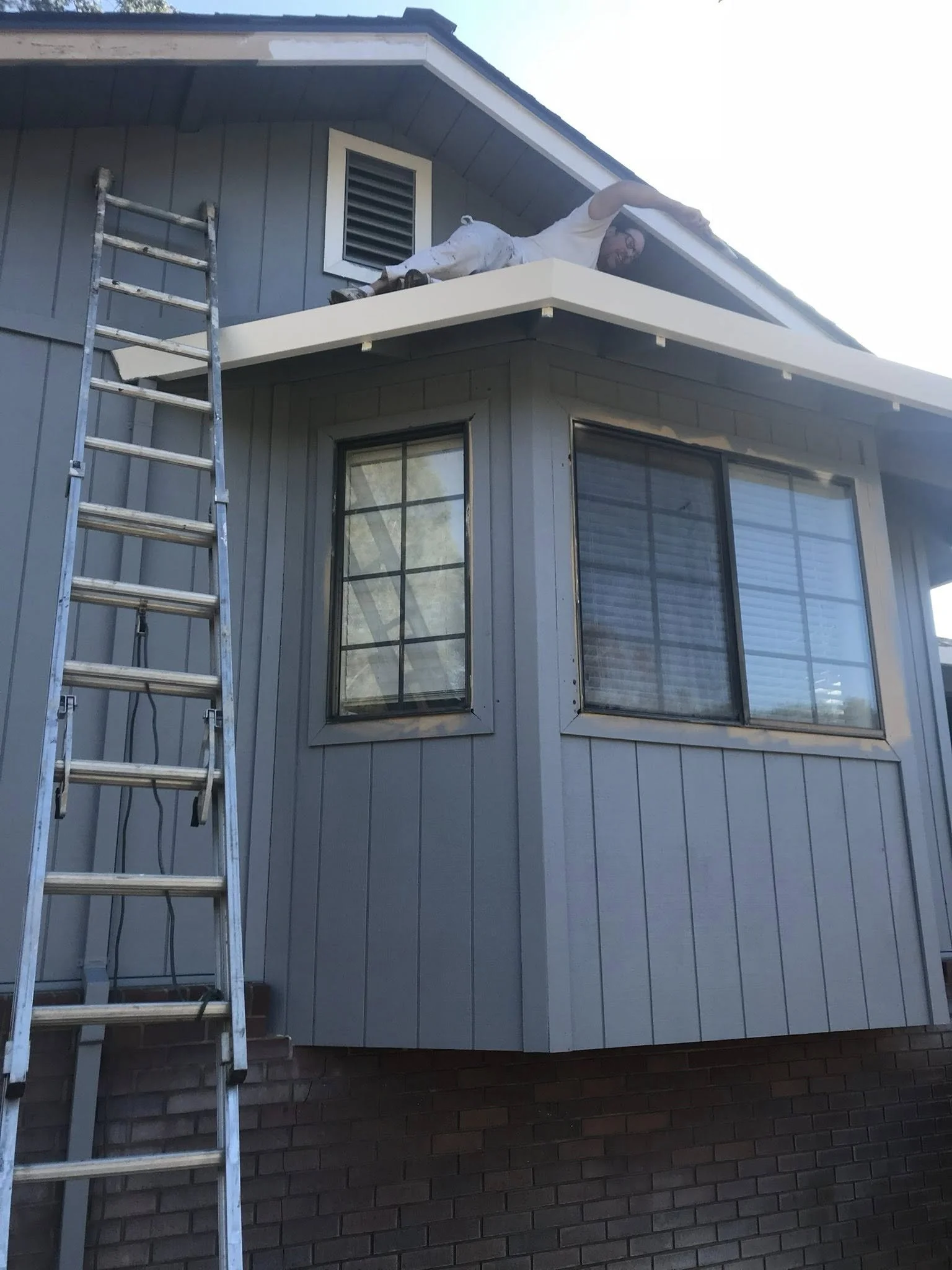 A man lying on the roof of a house, next to a ladder, working or inspecting the building's edge.
