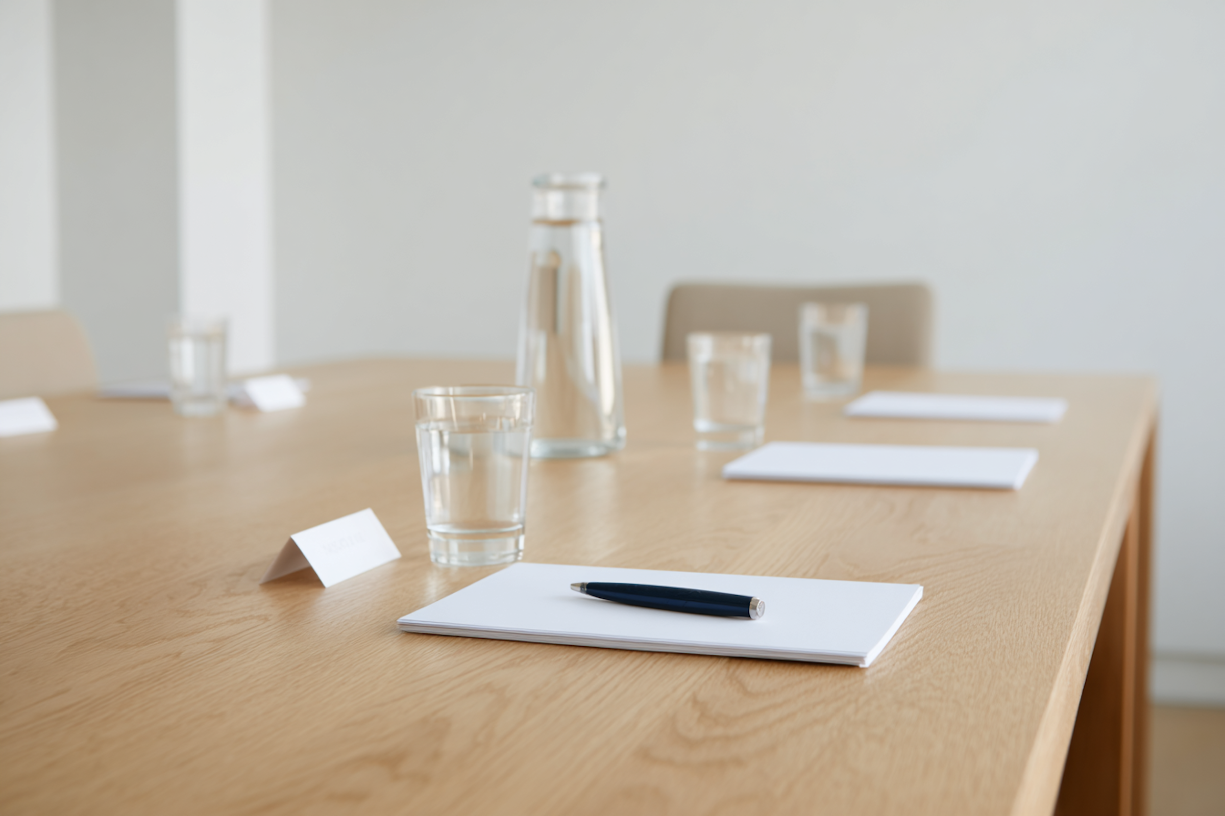 A conference room table with notepads, a pen, glasses of water, and a water pitcher.