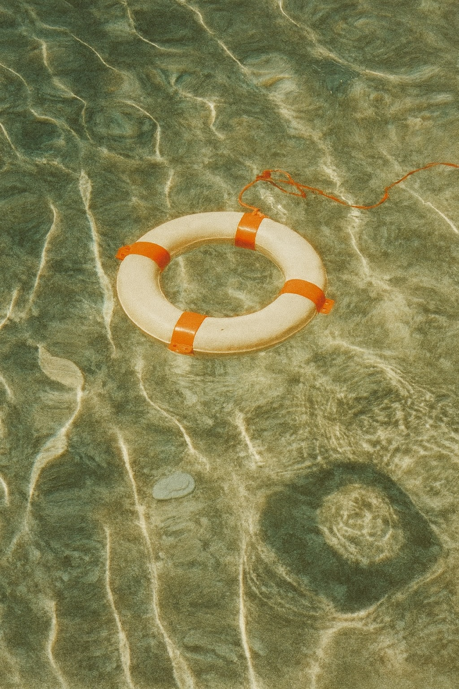 A life preserver floating upside down in shallow water with a rope attached, near the sandy or rocky bottom.