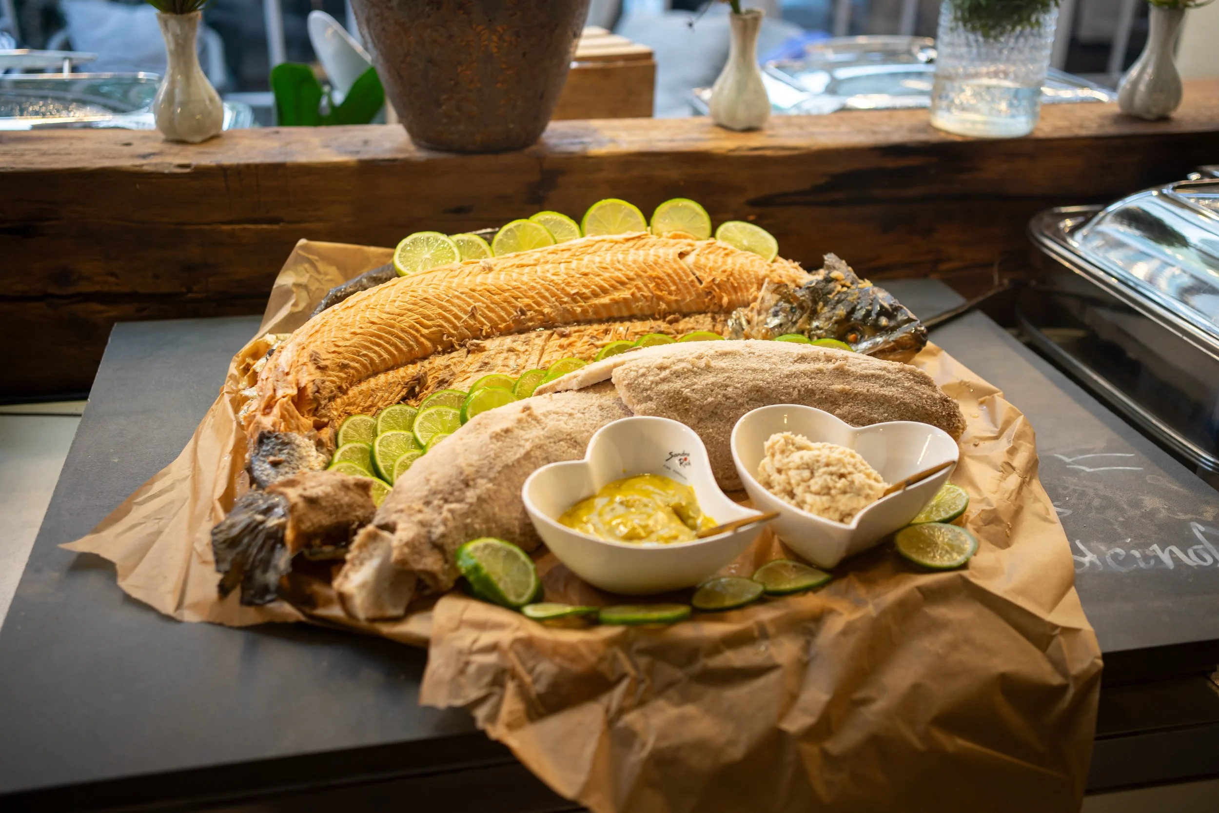 Fischplatte mit Garnelen, Limonen, Saucen und Beilagen auf braunem Papier in einer stilvollen Umgebung.
