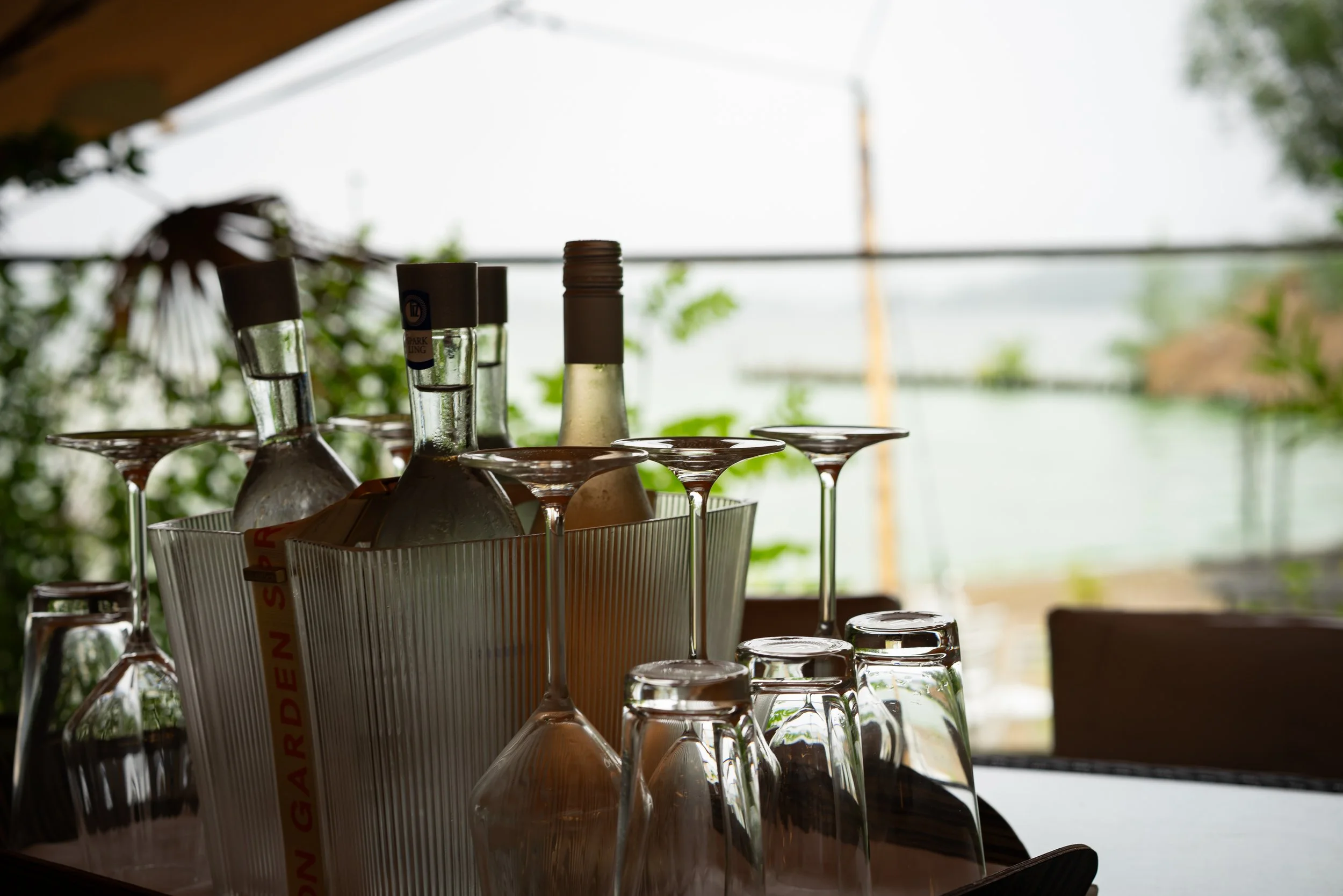 Leere Wein- und Cocktailgläser stehen in einer Kiste auf einem Tisch im Restaurant, im Hintergrund ist eine Fensterfront mit Blick auf die Natur draußen.