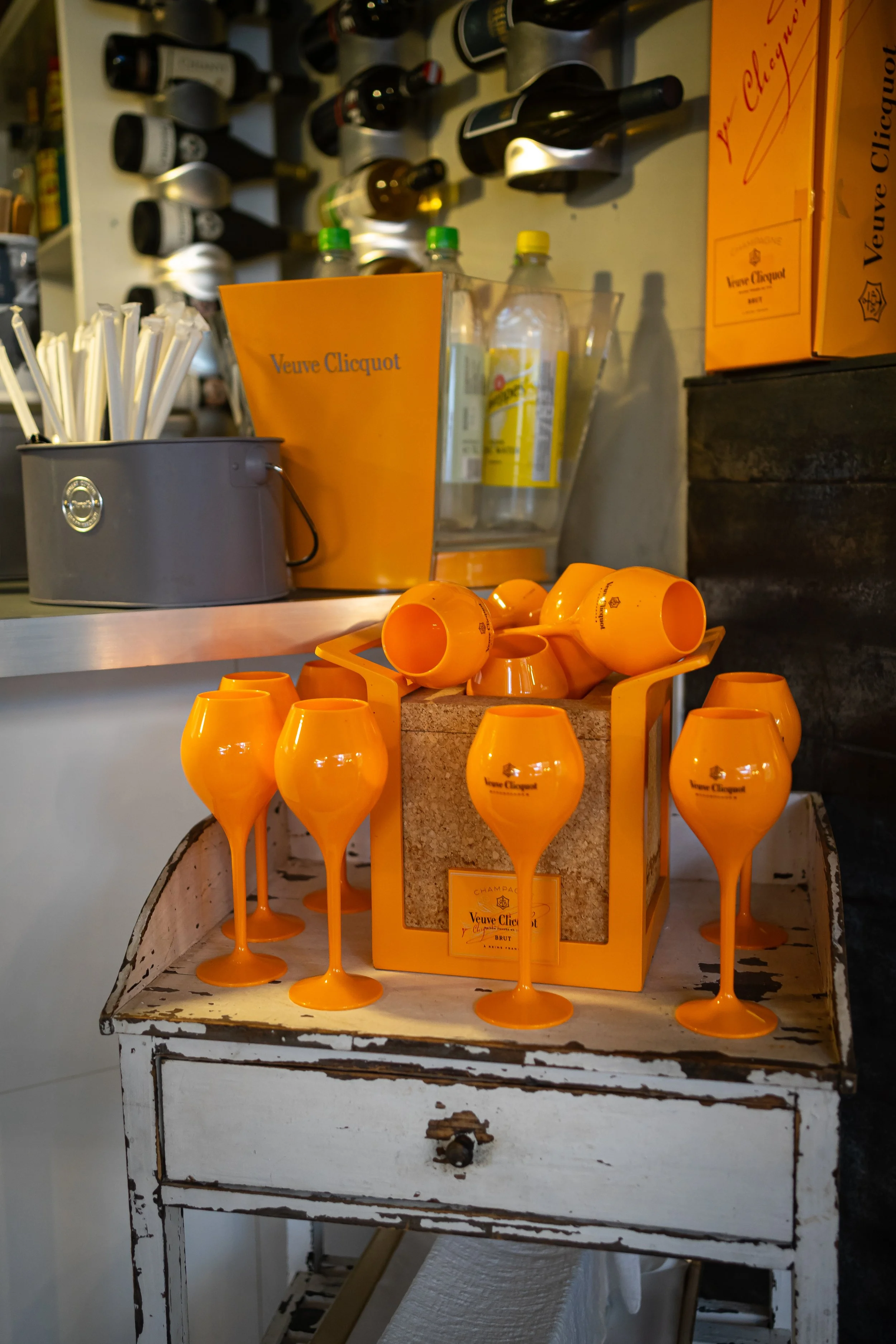 Orange Weingläser und Champagnerkühler mit Veuve Clicquot branding. Im Hintergrund regale mit Weinflaschen.