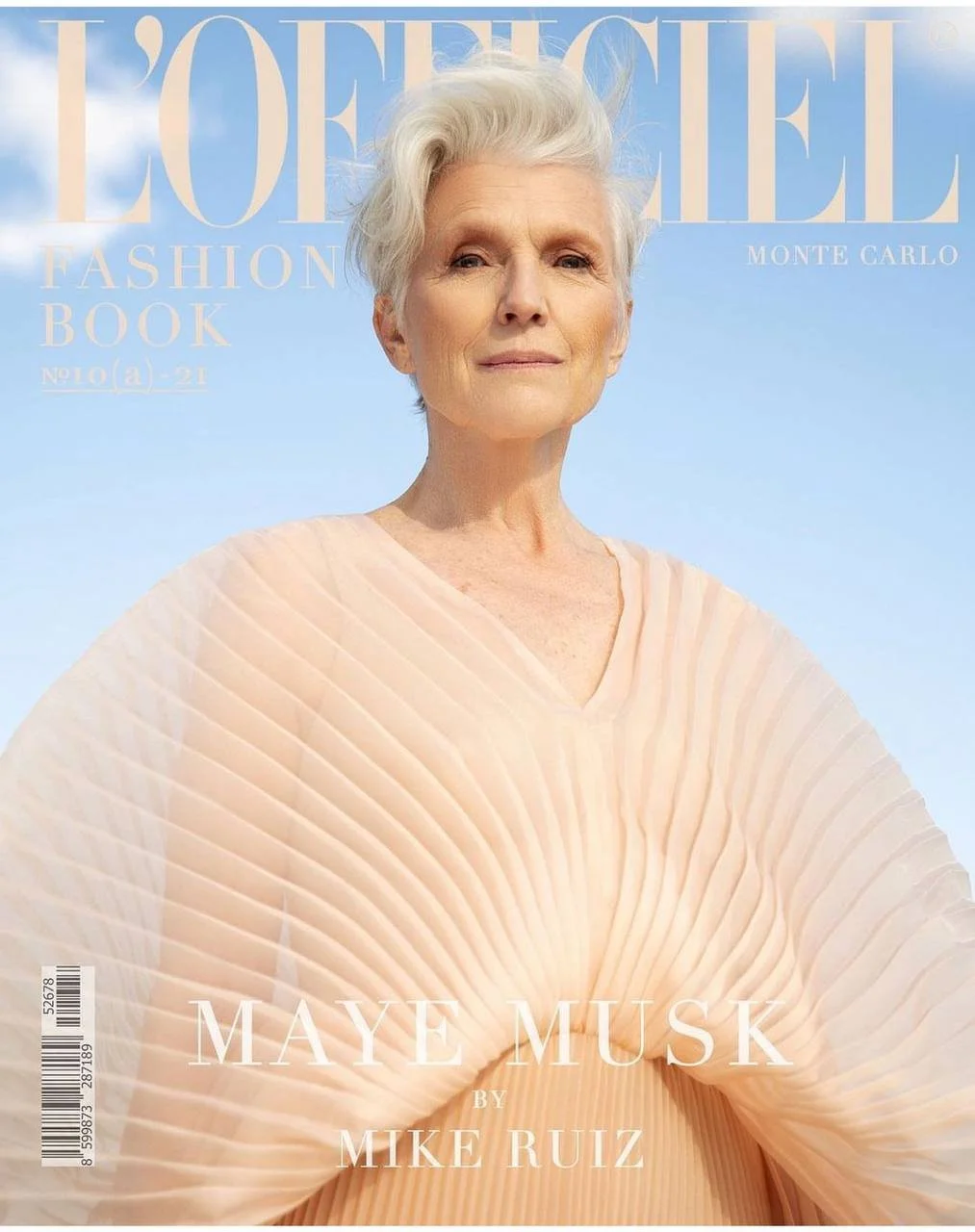 Magazine cover featuring Maye Musk with short, platinum blonde hair, wearing a beige pleated top, against a blue sky background.